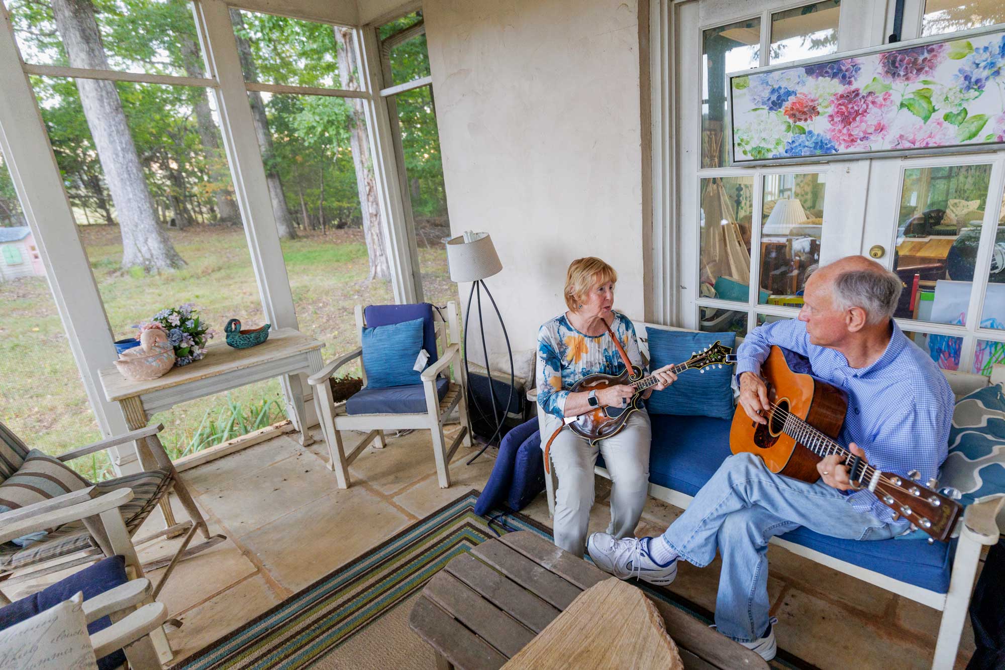 Dr. Pinkerton and Alan Pinkerton sitting in their closed-in porch playing music together. Dr. Pinkerton plays the mandolin and Alan plays the guitar.