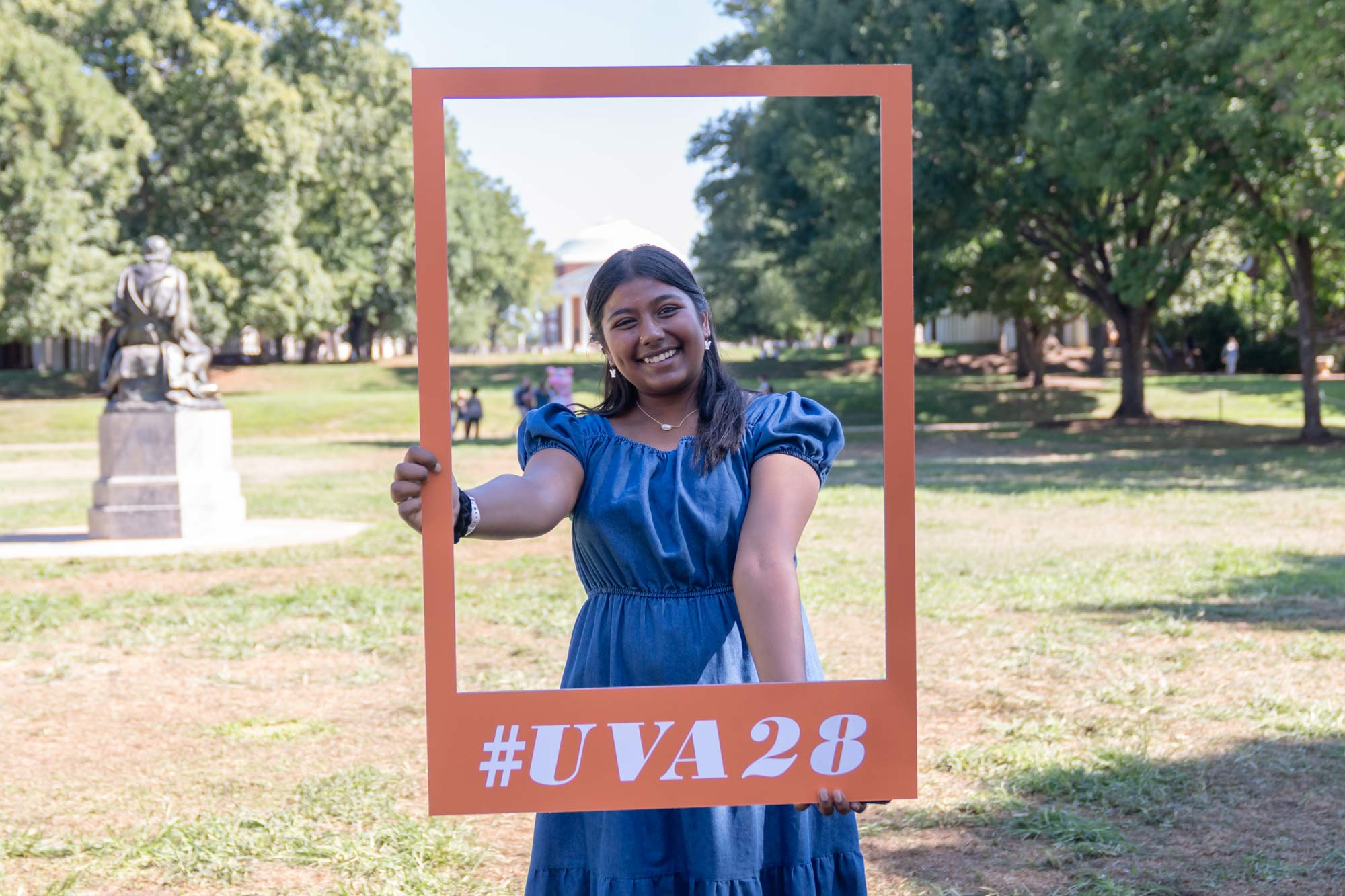 a student poses with a frame saying "#UVA28" on the Lawn in front of the UVA Rotunda