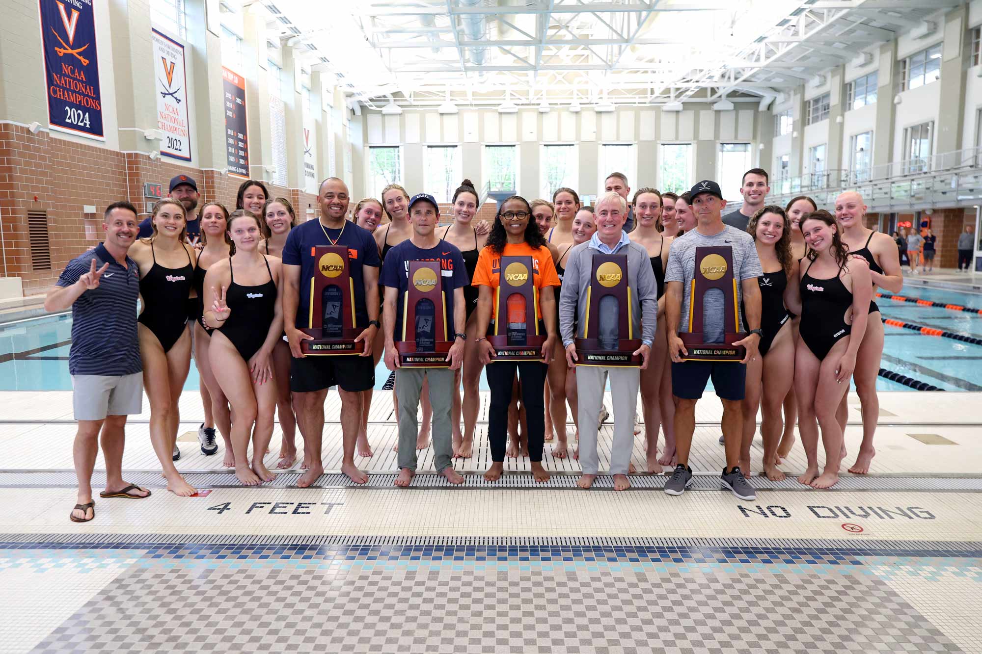 A portrait of the UVA swim team in swimsuits, proudly holding a trophy.