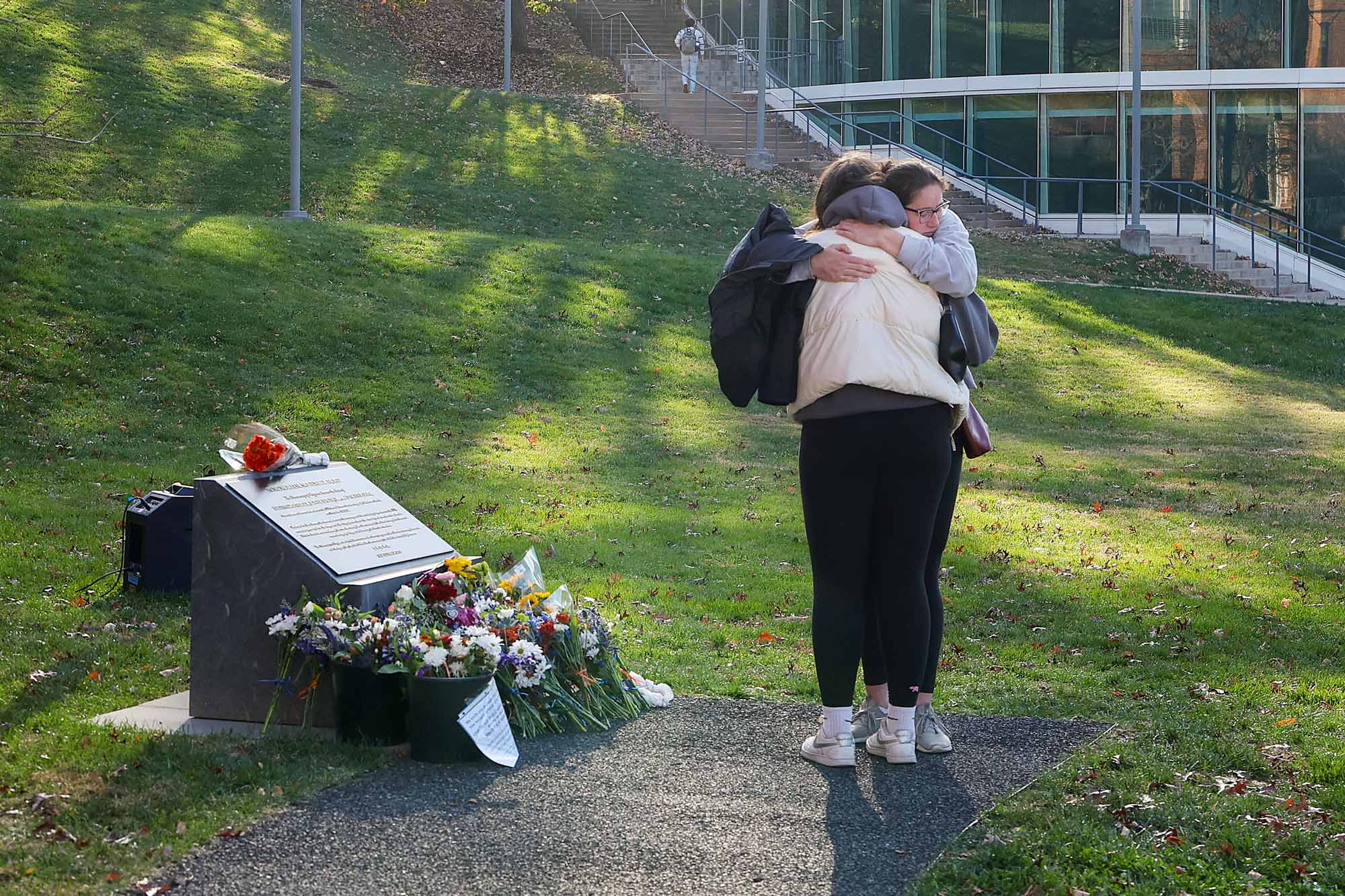 Izzie Bird and Lauren Benedict hugging in front of the UVA memorial statue