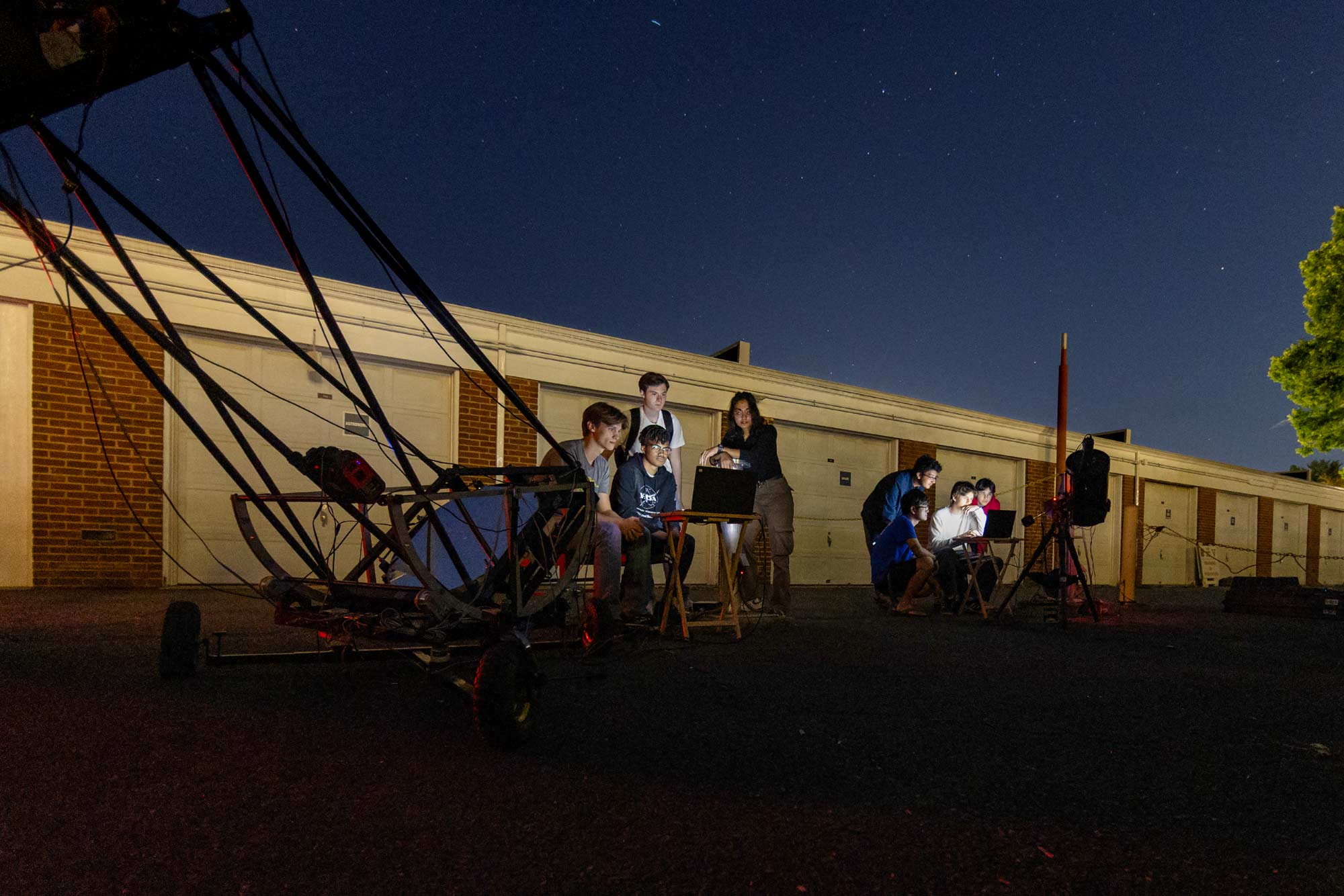Portrait of Groups of students follow their tracking on two computers while monitoring space with two telescopes from the Grounds.