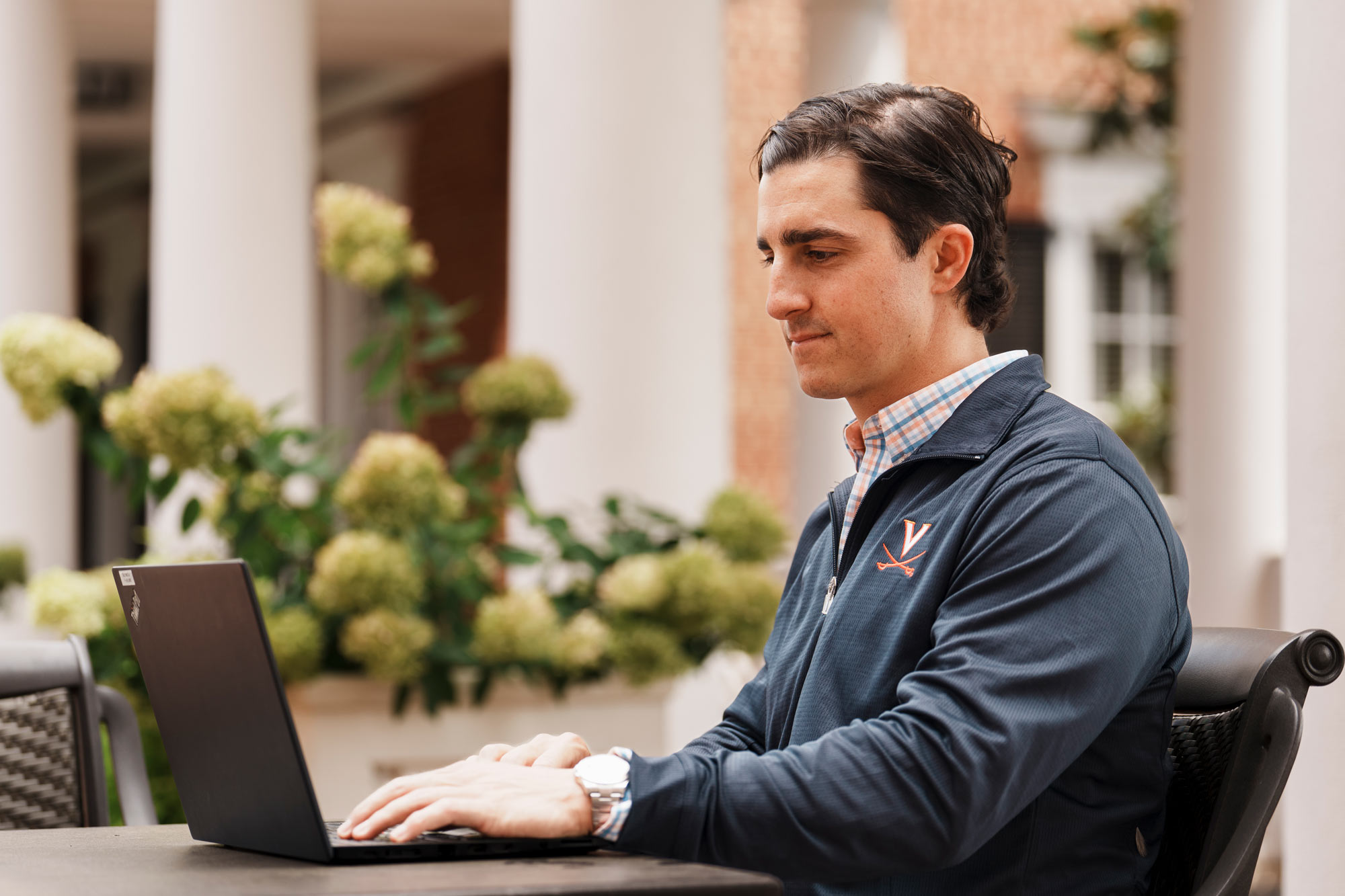 Andrew Katz working on a laptop sitting in a courtyard at the Darden School of Business at UVA
