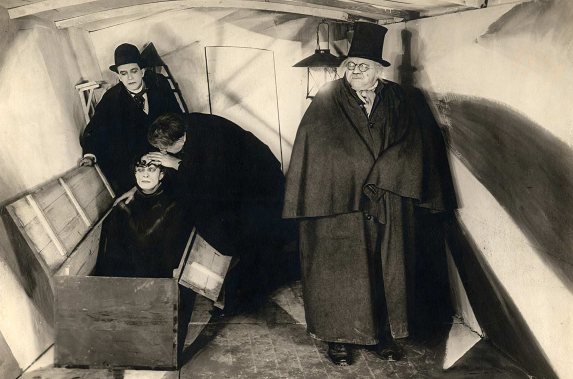 A scene from The Cabinet of Dr. Caligari showing three men and a somnambulist rising from a box in a distorted room.