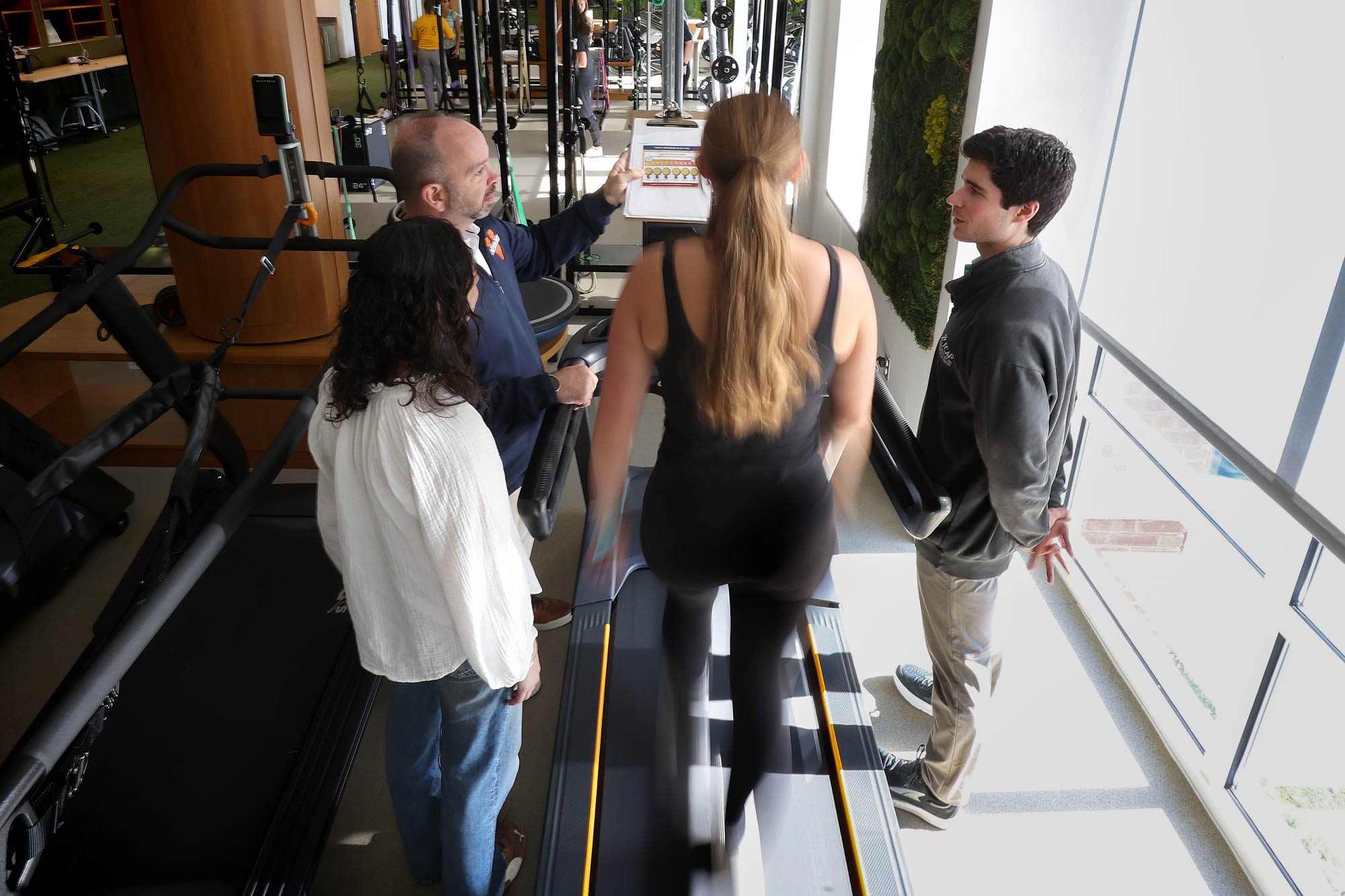 Jake Resch monitoring a student on a treadmill and speaking to other specilaists