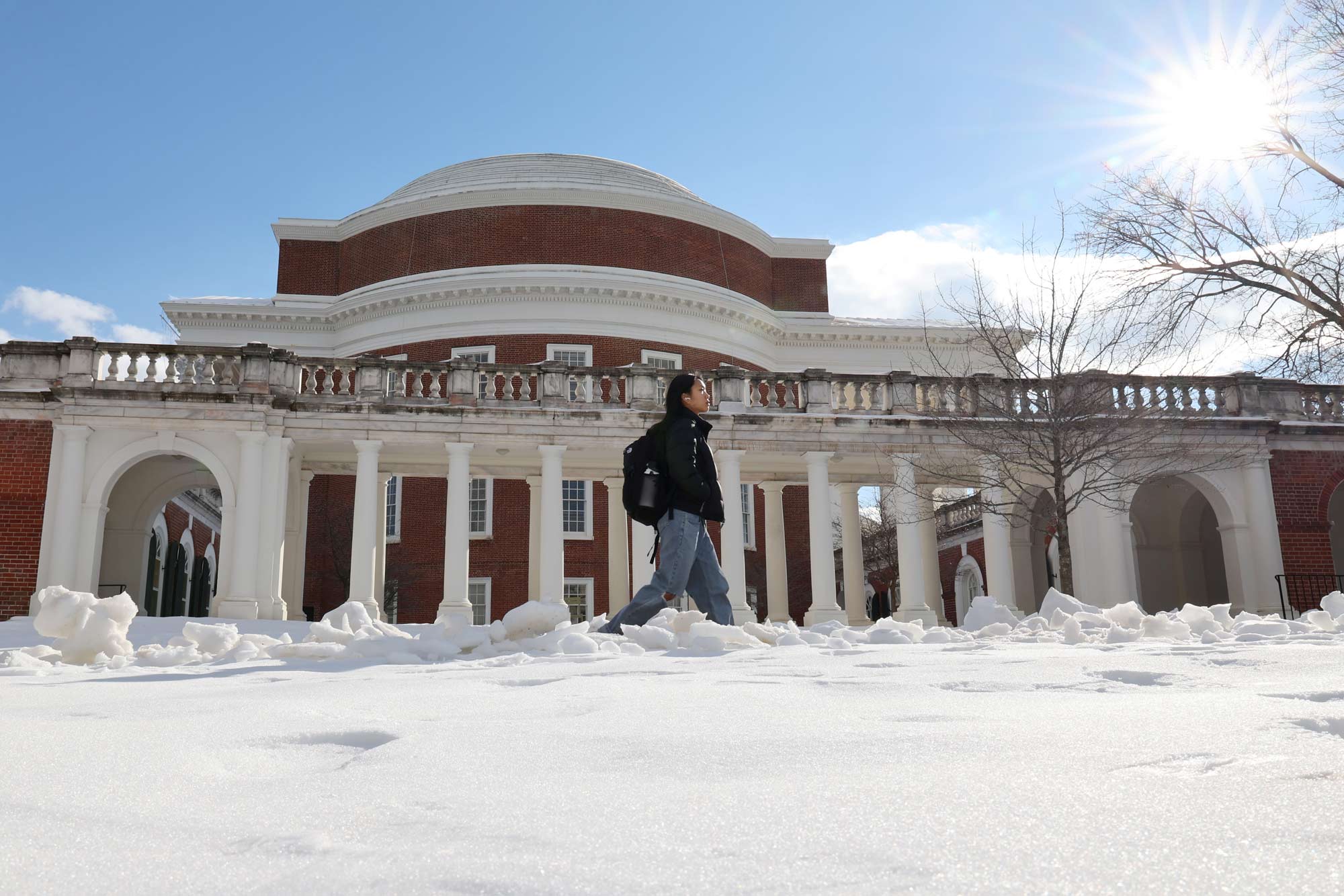 A student walks by the side of the Rotunda with a layer of snow coating the ground