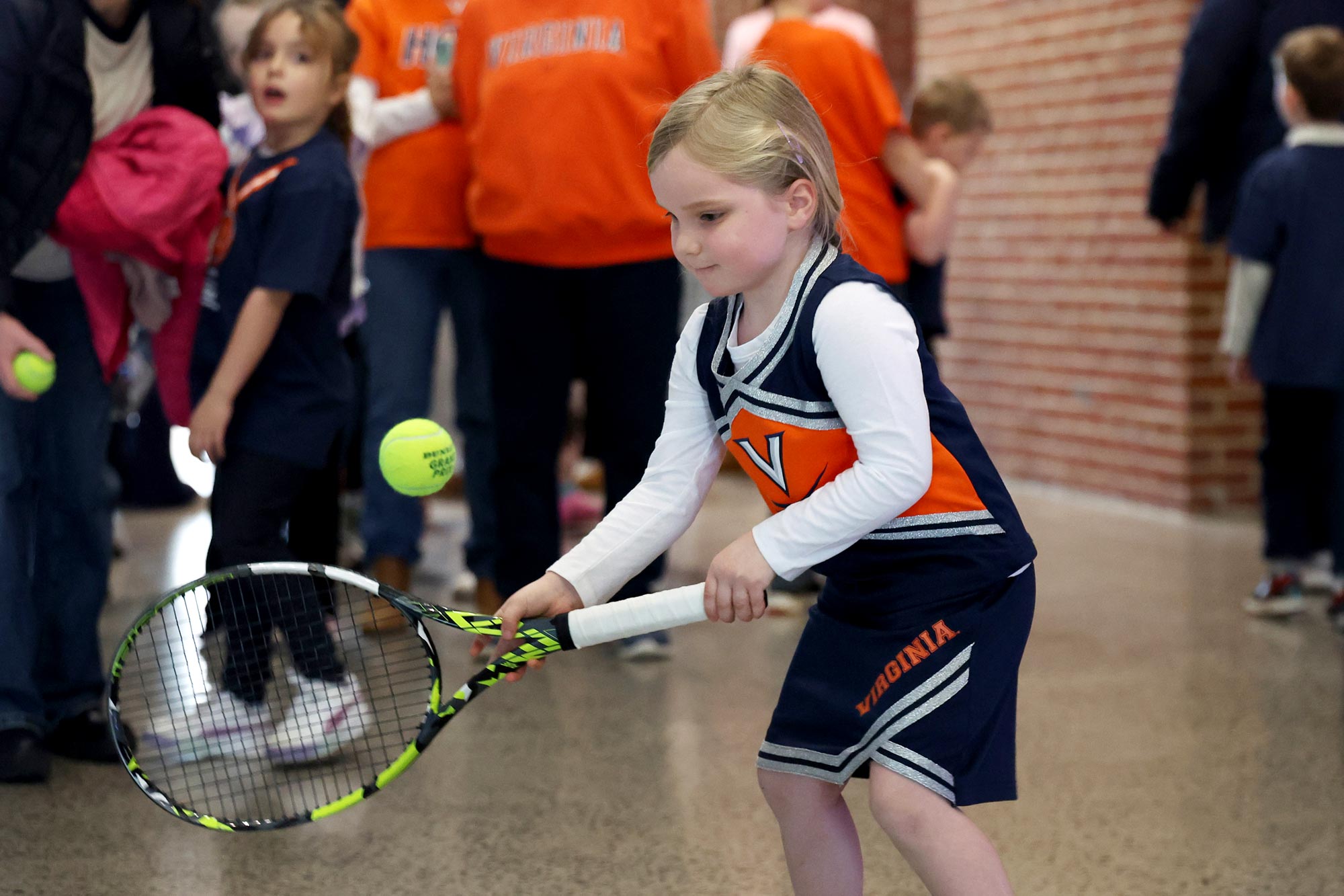 A young UVA fan, decked out in orange and blue, takes a swing at learning tennis.