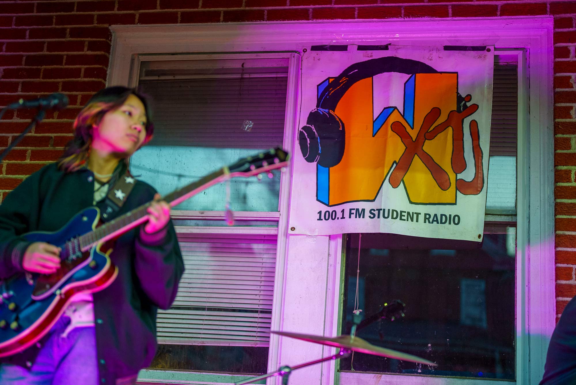 a WXTJ banner in the style of MTV's logo hangs over a window while a band plays on a front porch