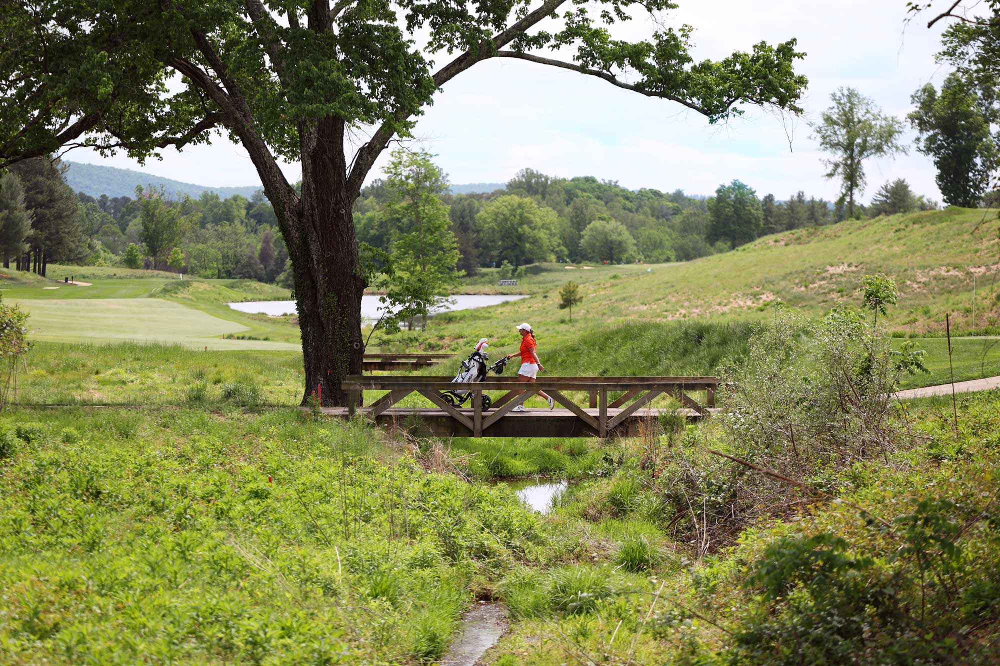 Jaclyn LaHa walking her golf bag across a bridge at the Boar’s Head course