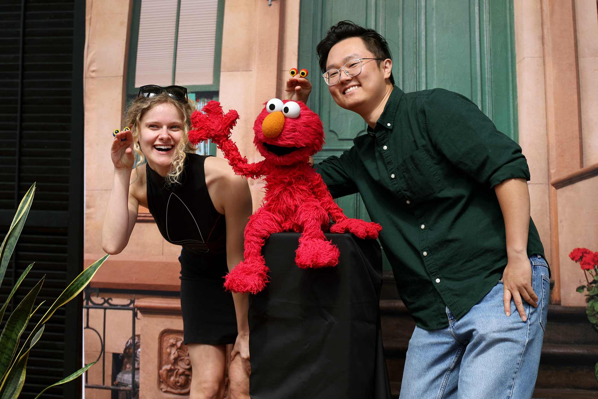 Two people posing with Elmo in front of a Sesame Street backdrop.