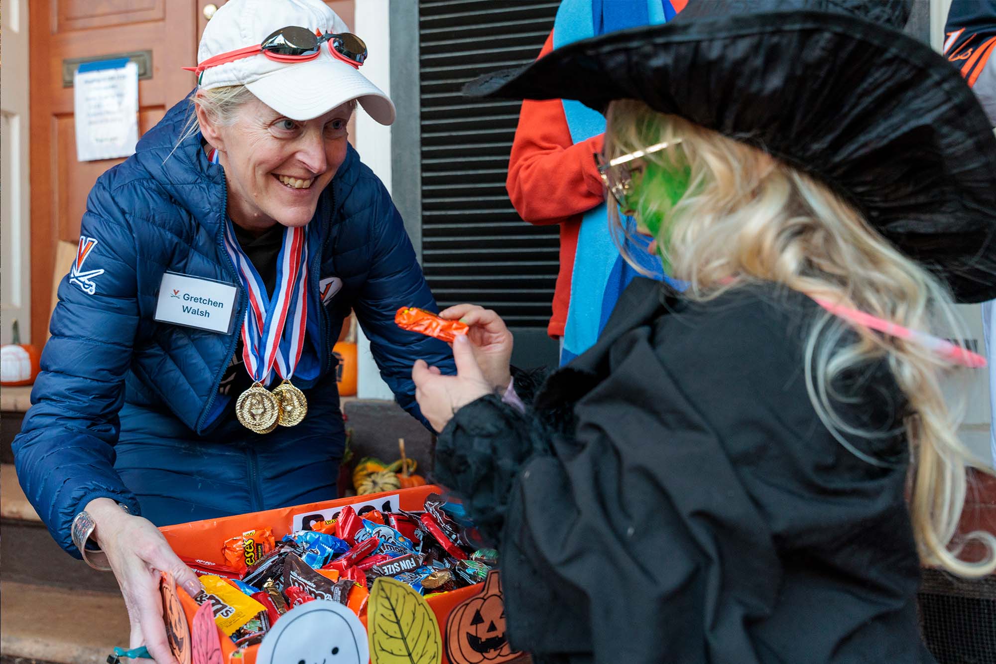 Jennifer “J.J.” Wagner Davis, UVA’s Executive Vice President and Chief Operating Officer, dressed as UVA alum and Olympian Gretchen Walsh hands out candy to a child dressed as a witch.