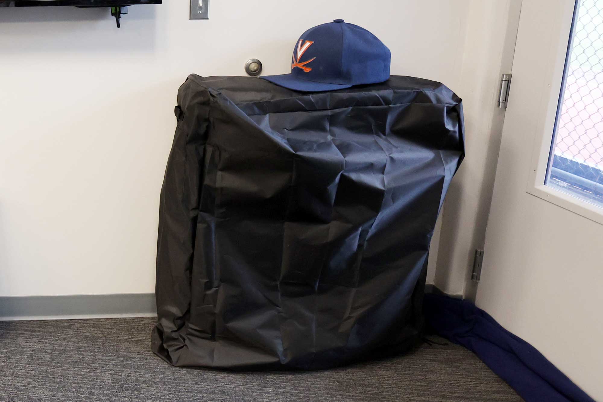 A UVA baseball hat sitting on top of a foldable bed sitting in a corner.