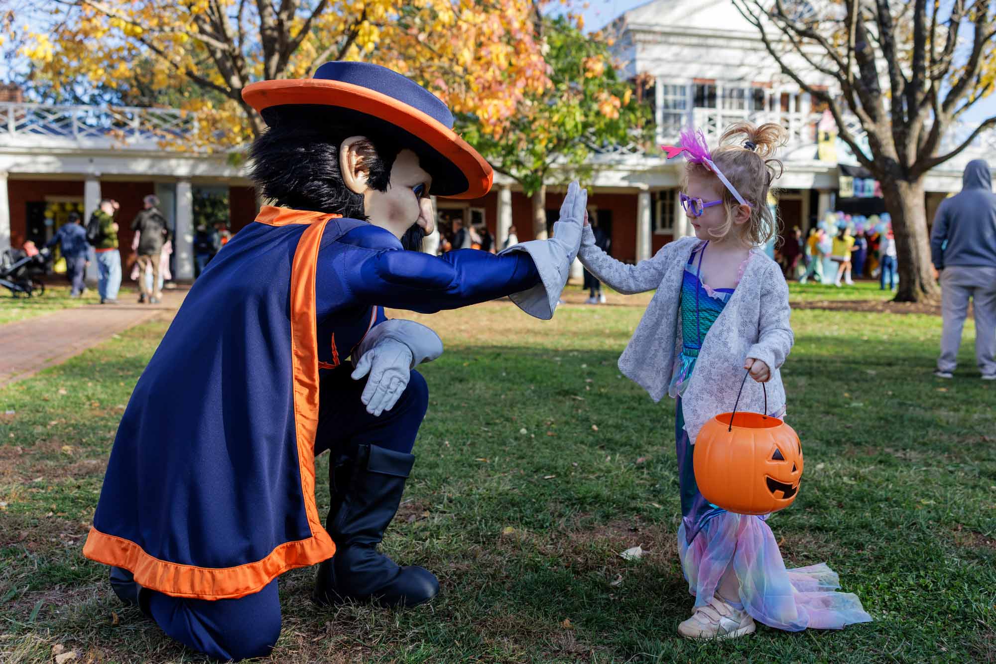 Cavman high-fives a young girl dressed as a mermaid holding a plastic pumpkin to collect her treats from Trick-or-Treat on the Lawn.