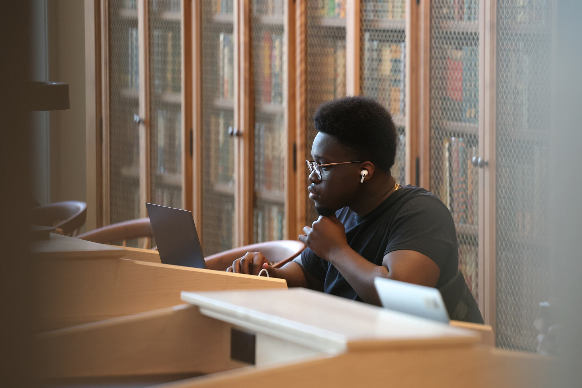 A student listens to music and studies at a wooden desk in the Shannon library