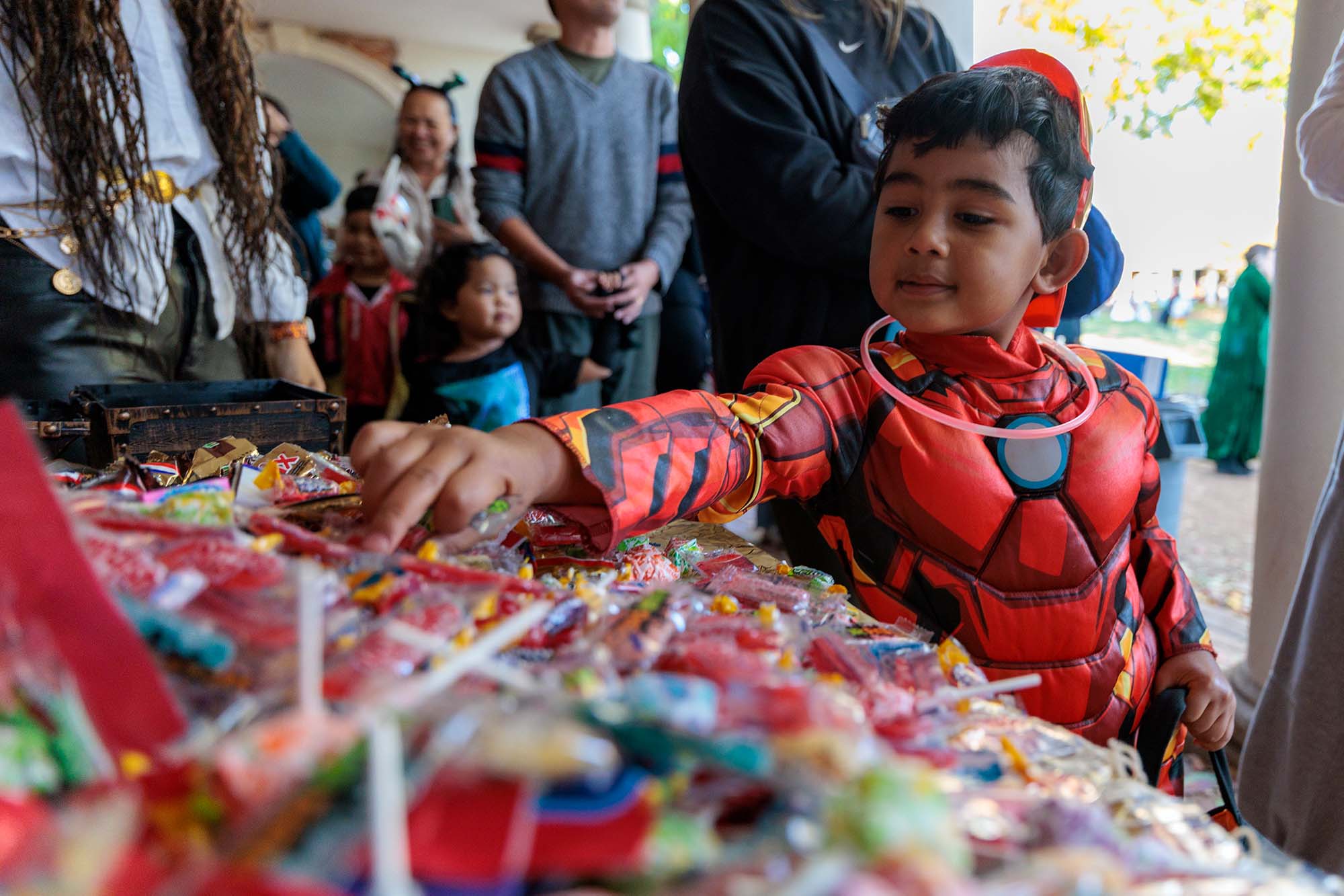 A young boy dressed as Iron Man makes his selection from a table filled with candy.