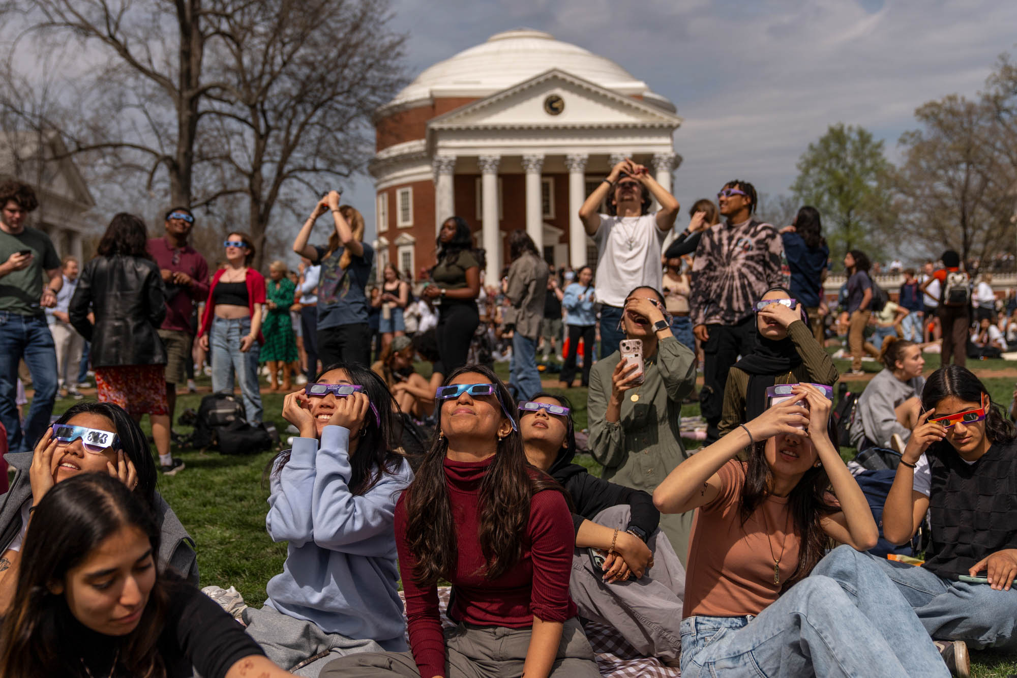 Several students wear eclipse viewing glasses and look up at the eclipse on the Lawn with the Rotunda in the background