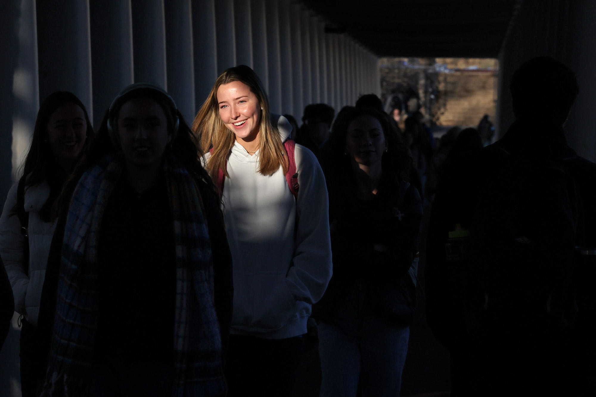 The sun highlights a students face as they walk down an outdoor corridor 