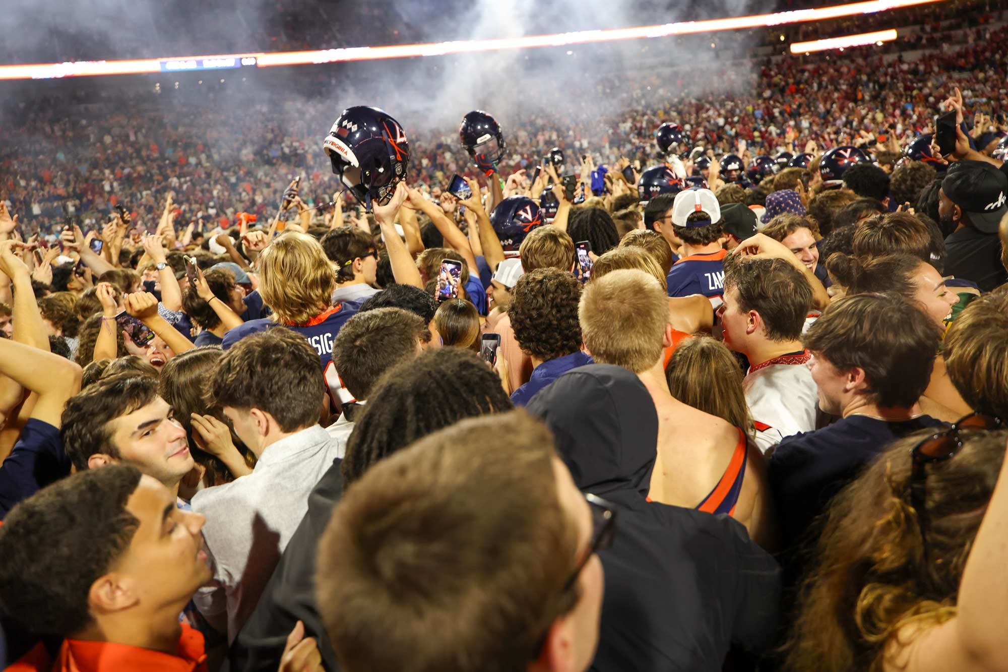 Picture of UVA football players, surrounded by the mass of fans who stormed the field, raise their helmets in celebration.