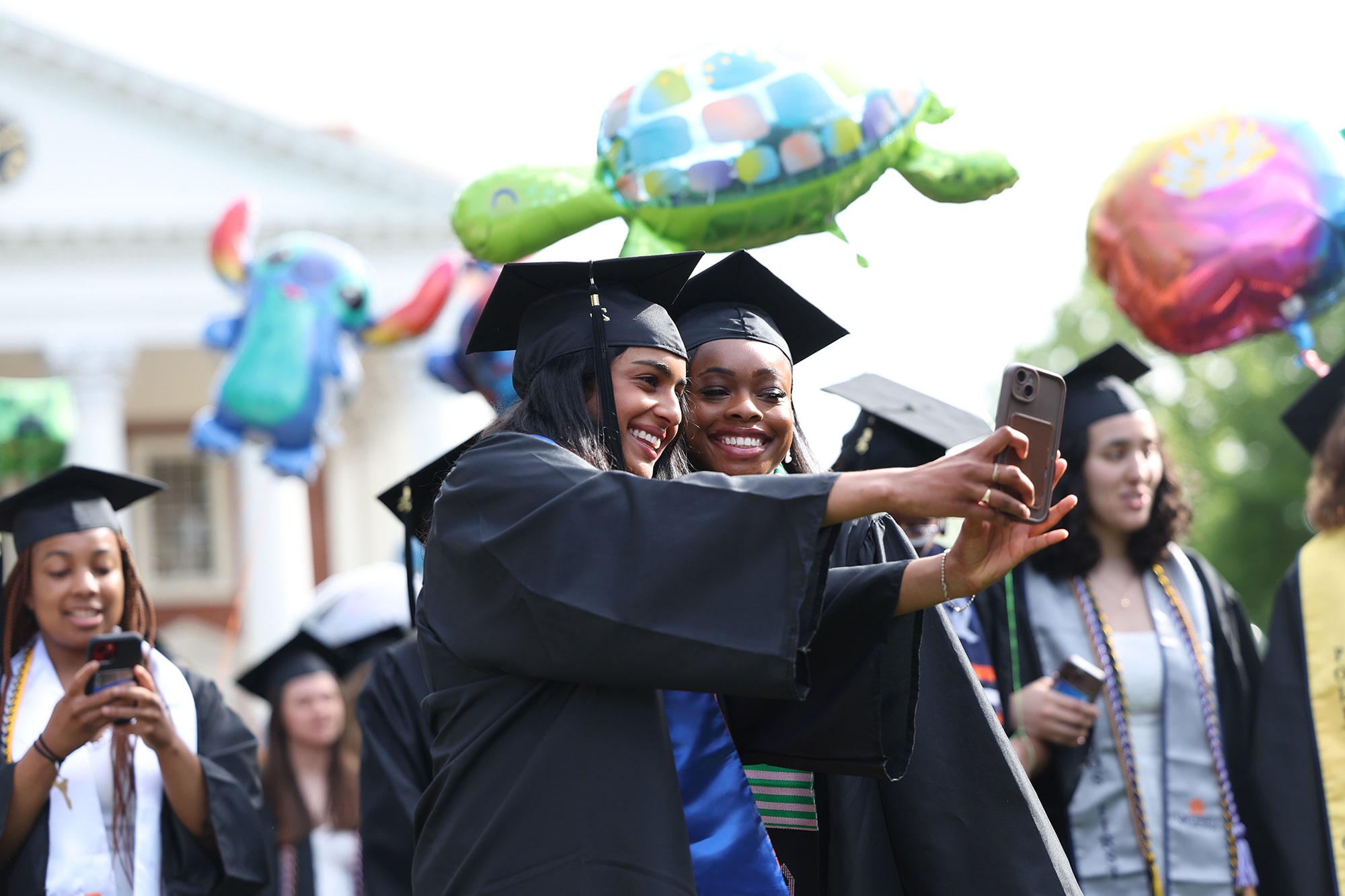 Two 2025 graduates take a selfie together while processing the Lawn