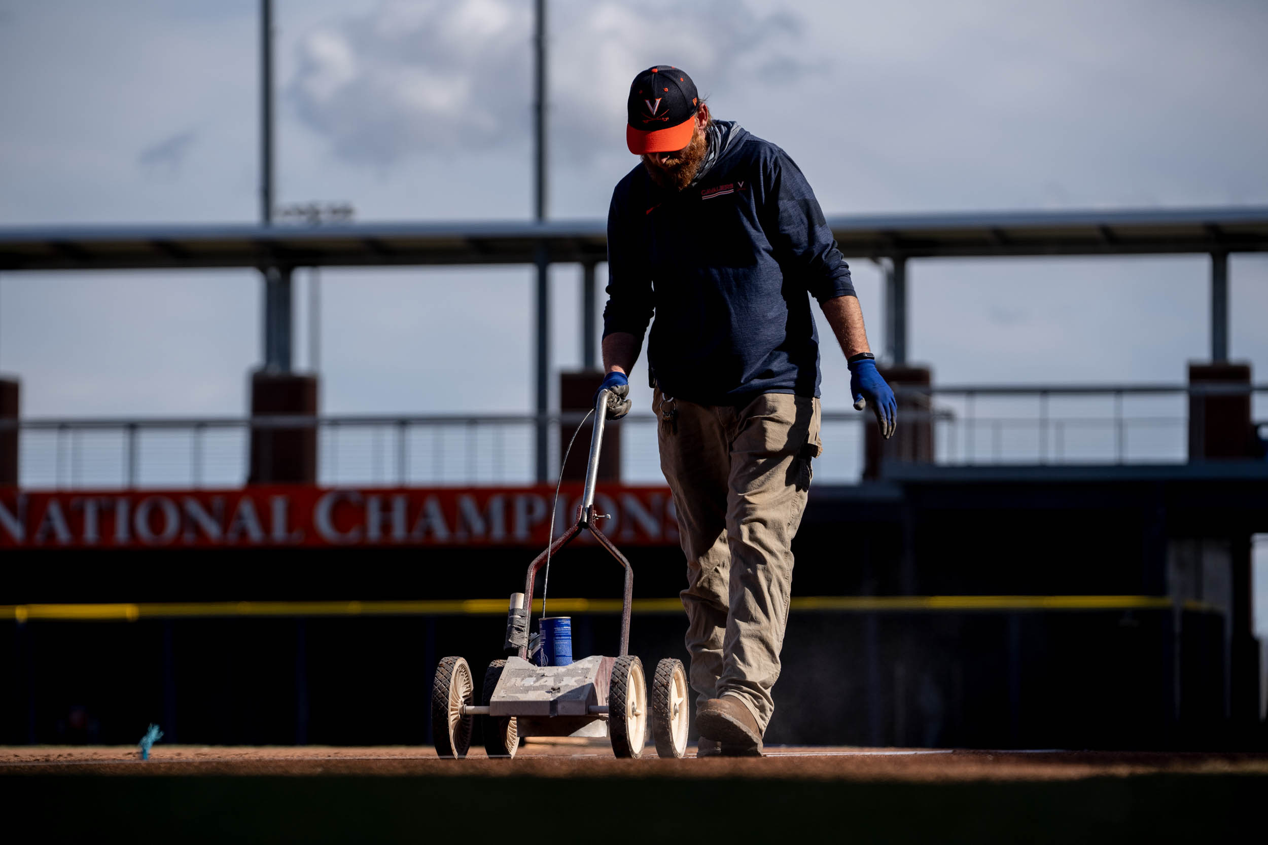 UVA Staff Member pushing a spray paint machine to mark the lines on the baseball field