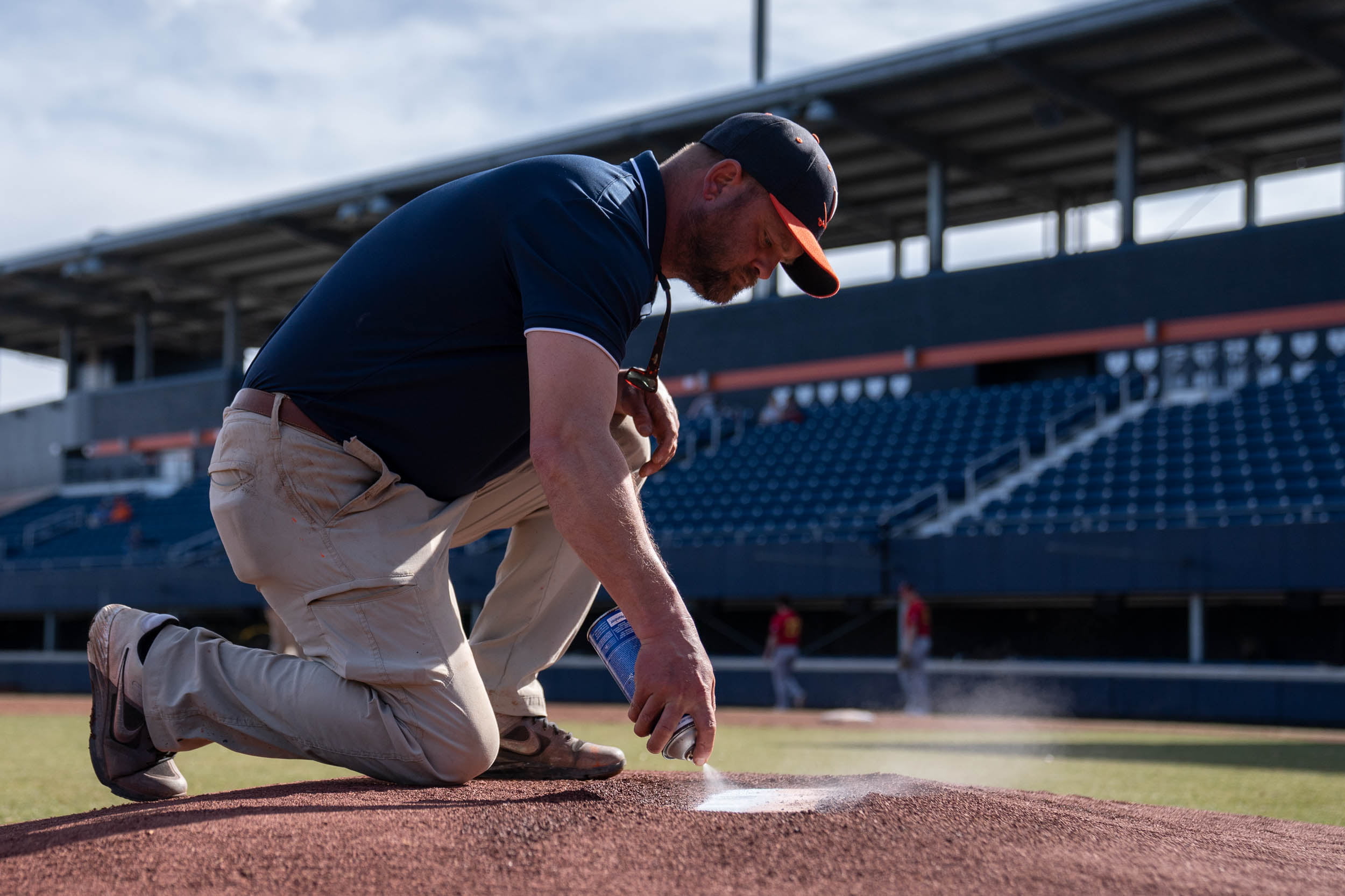 UVA Staff member kneeling down on the pitching mound spraying the mound