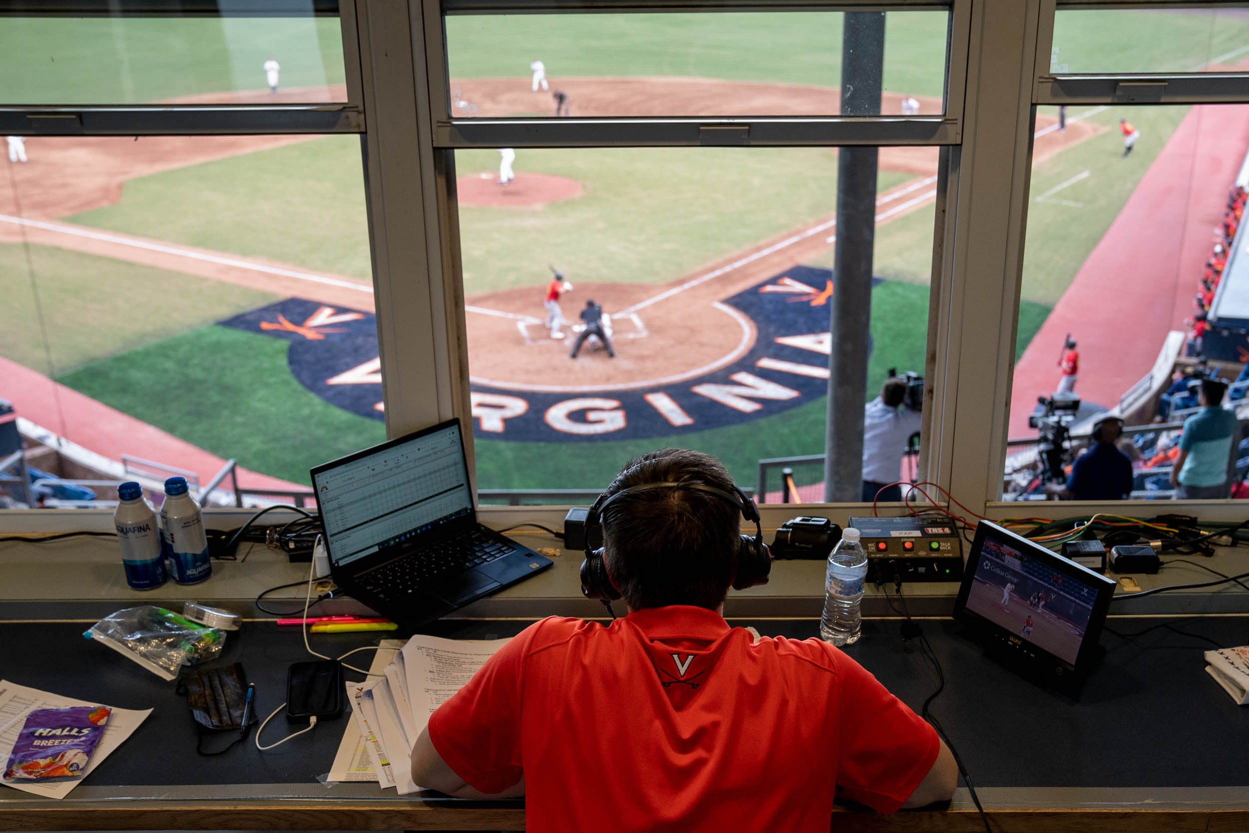 Announcer sitting at a desk behind home plate watching a baseball game