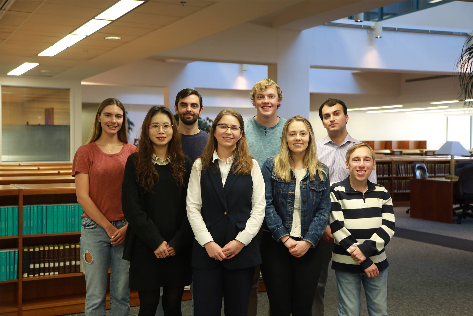 Olena Protsenko with Claudia Frykberg, Yali Liang, Stewart Lawrence, Justin Roberts, Megan Chapelle, Gregory Mekenian and Ryan Carp gathered around posing for picture in the Law Library