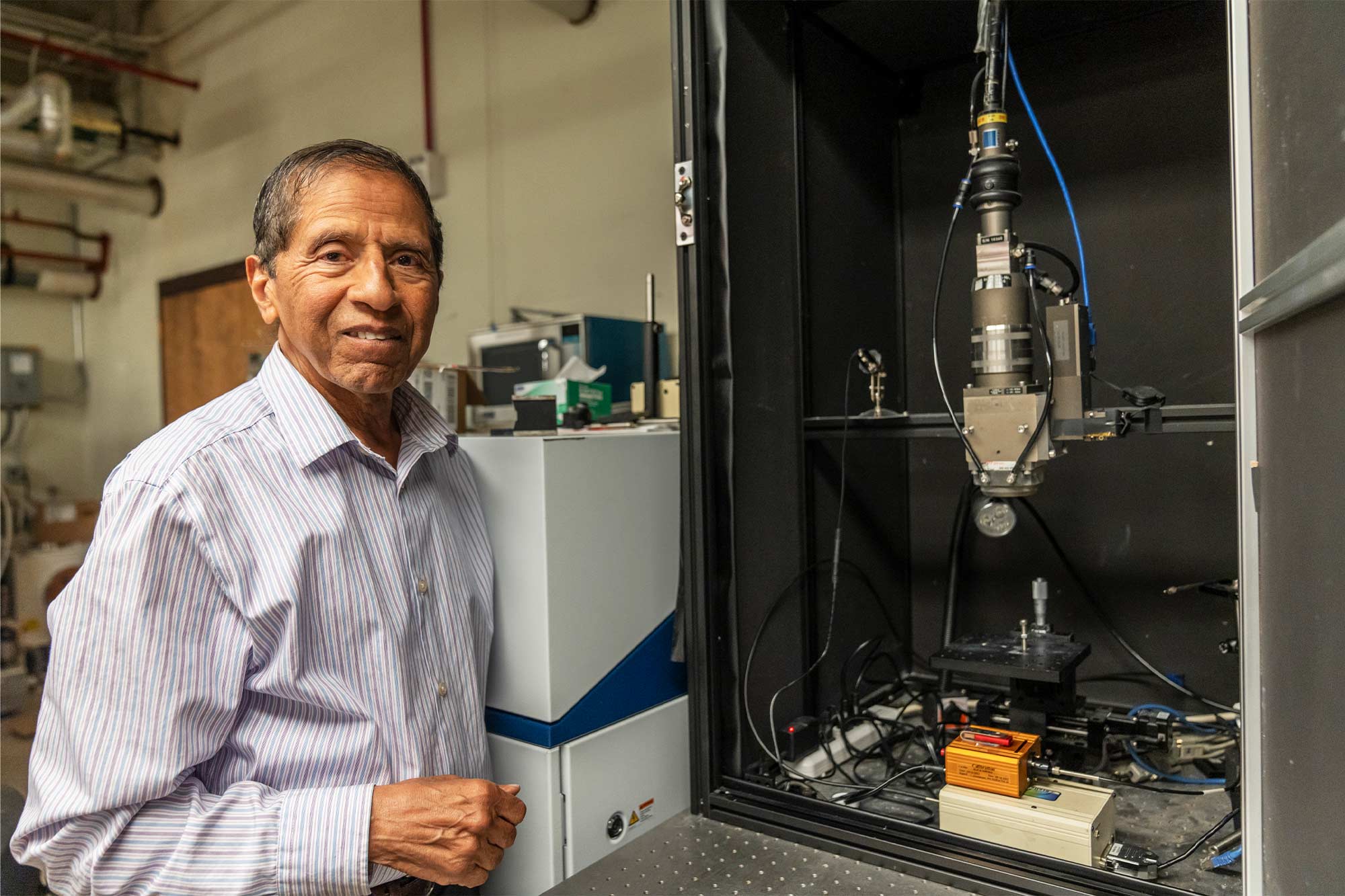 Mool Gupta stands next to a piece of machinery and looks at the camera