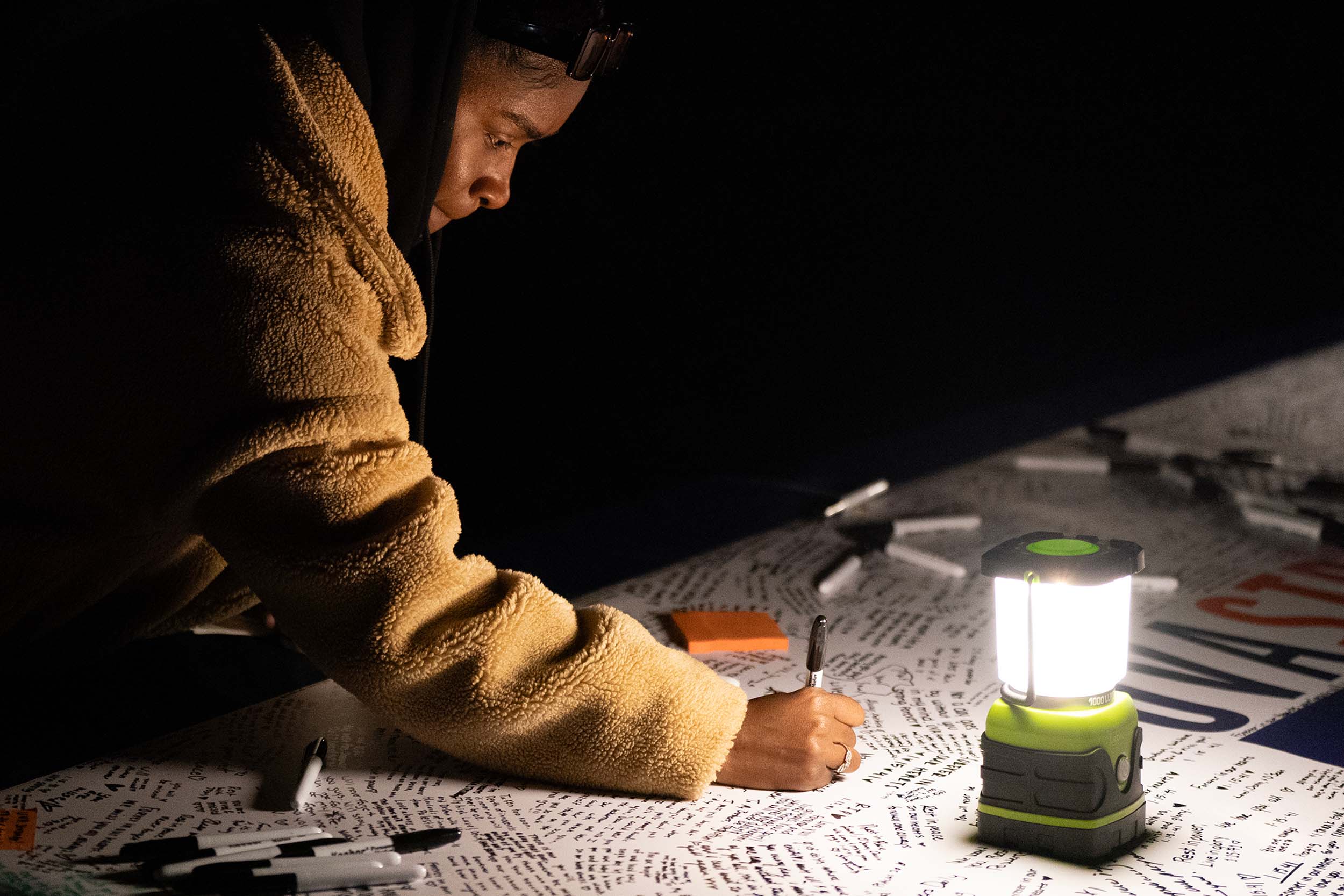 A student writing a message on the UVA Strong banner on the Lawn by the light of a lantern