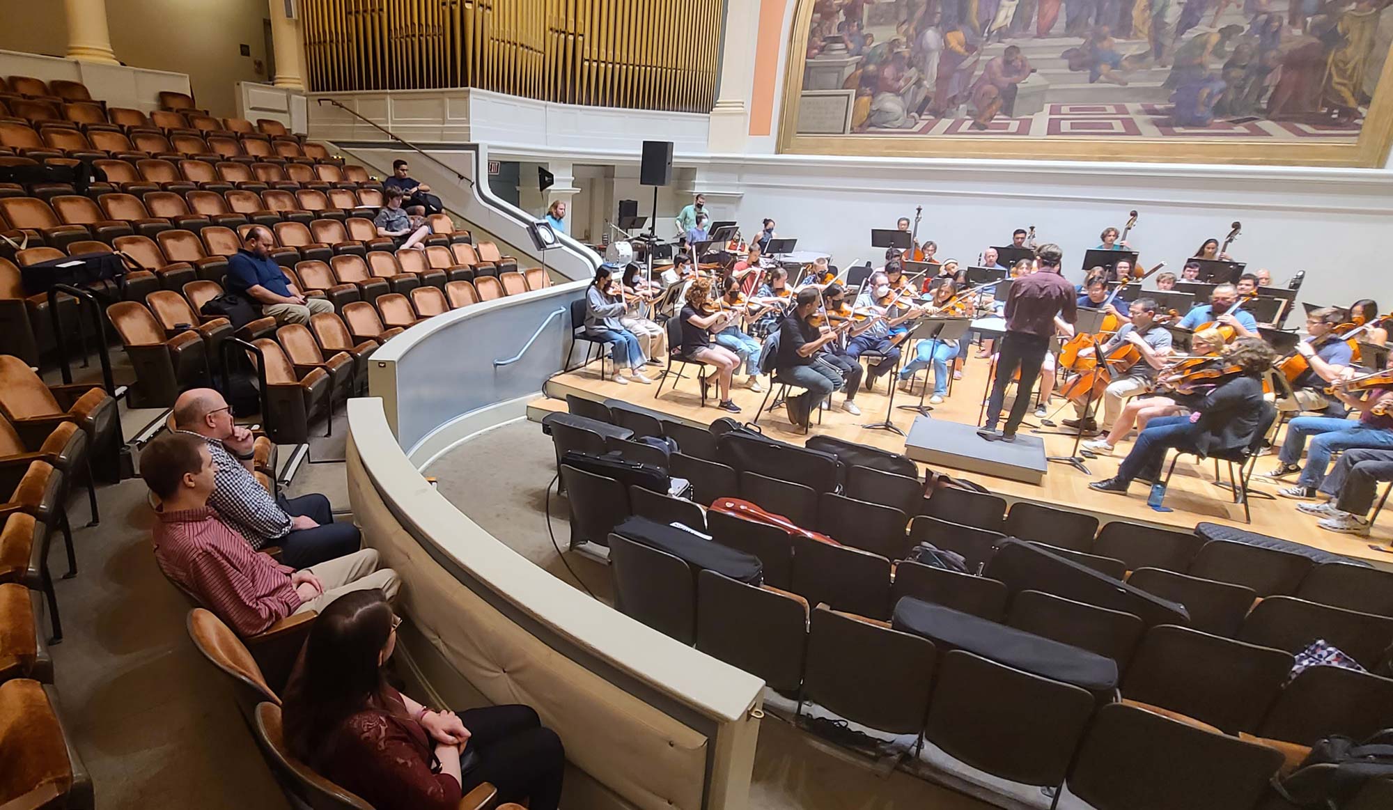 Several people are scattered amongst the auditorium seats, watching the symphony rehearse