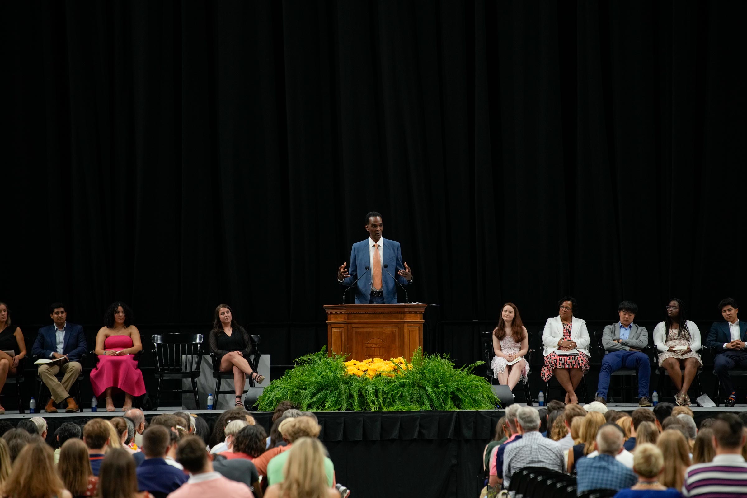 Ralph Sampson speaks from a podium on a stage flanked by the event's nine other speakers.