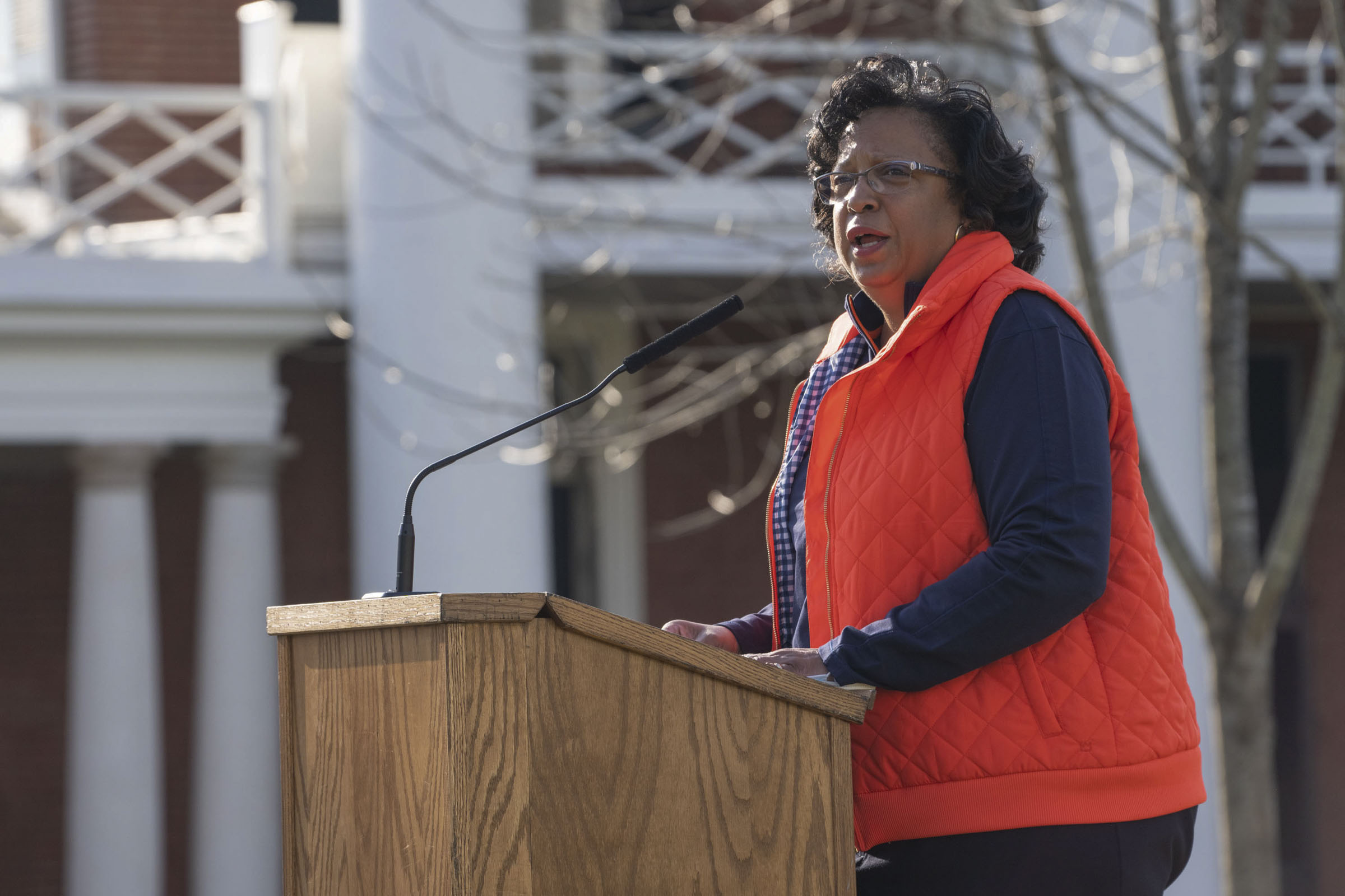 A woman in an orange vest speaks into a microphone at a podium