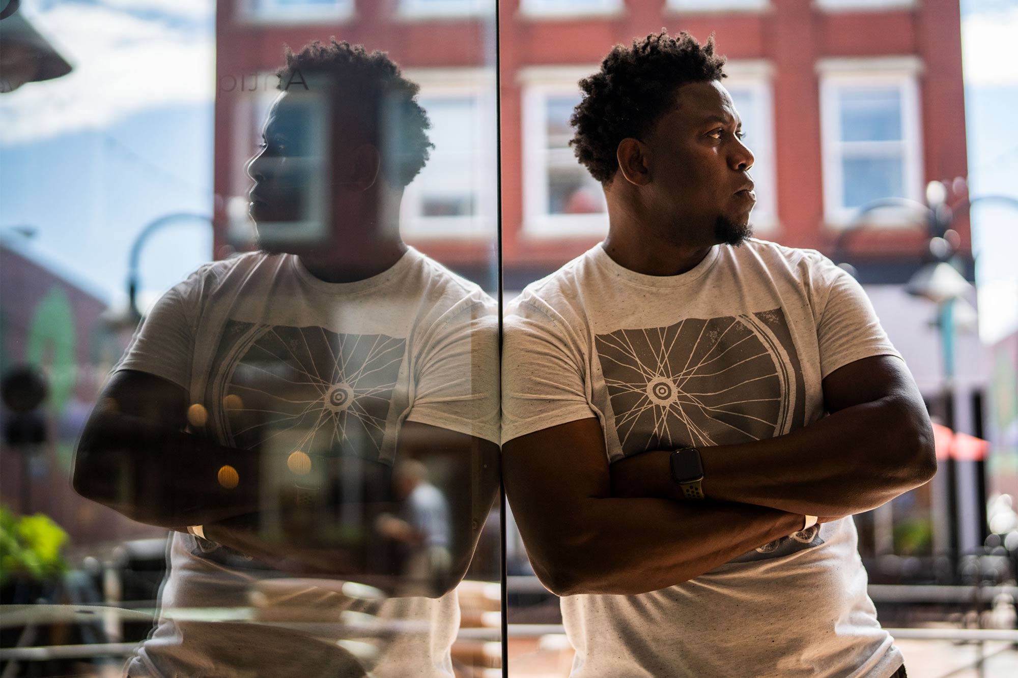 Eze Amos leans against a glass window, his reflection clear on the left.