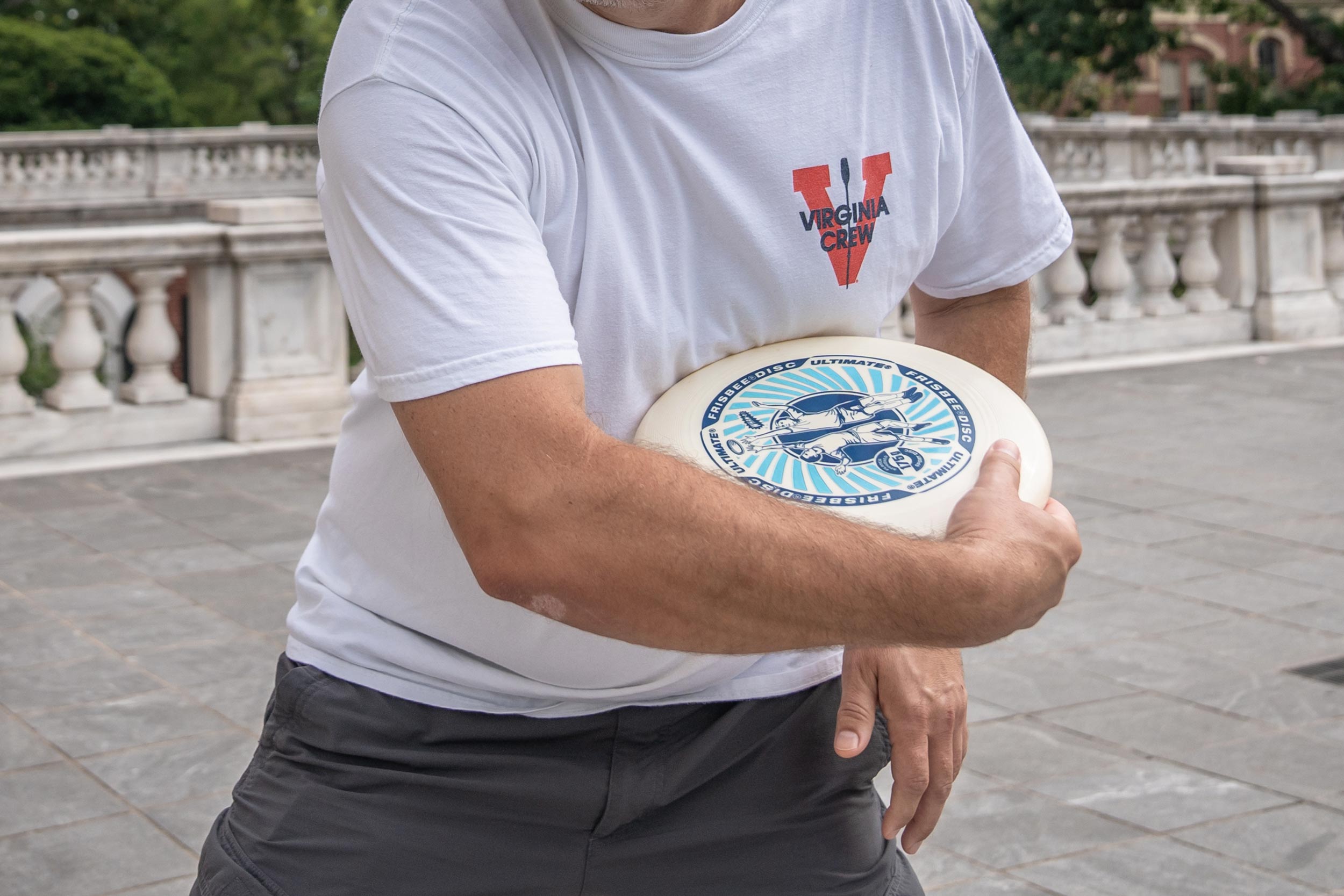 Close up of a man about to throw a frisbee while wearing an old U V A rowing shirt