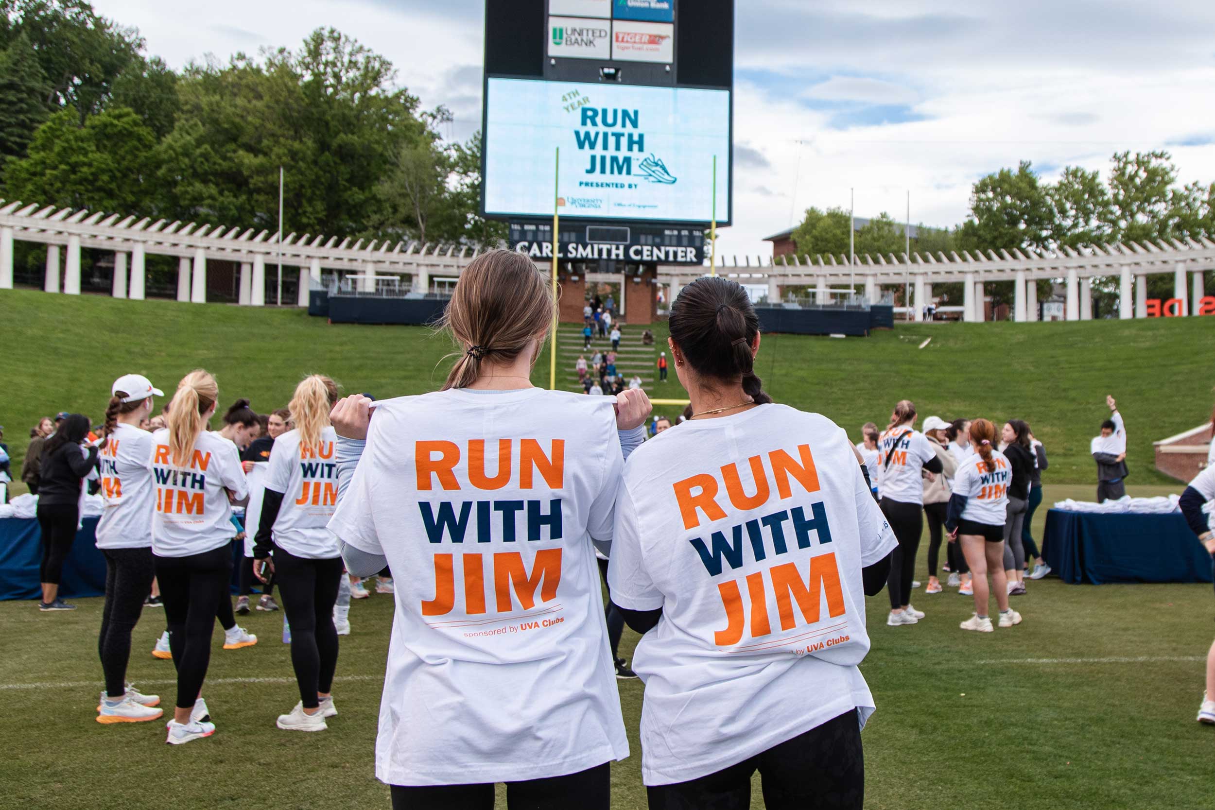 Two students face away from the camera showing off their "Run with Jim" shirts