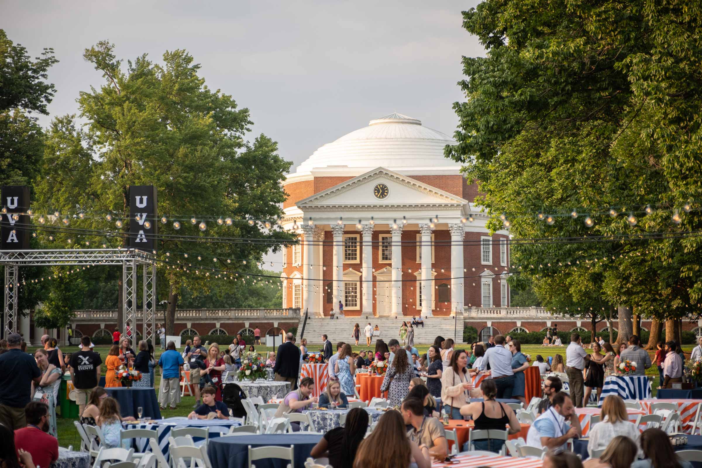 A reunion gathering on the lawn with the Rotunda in the background and nice bulb lights surrounding the picnic tables that alumni sit at