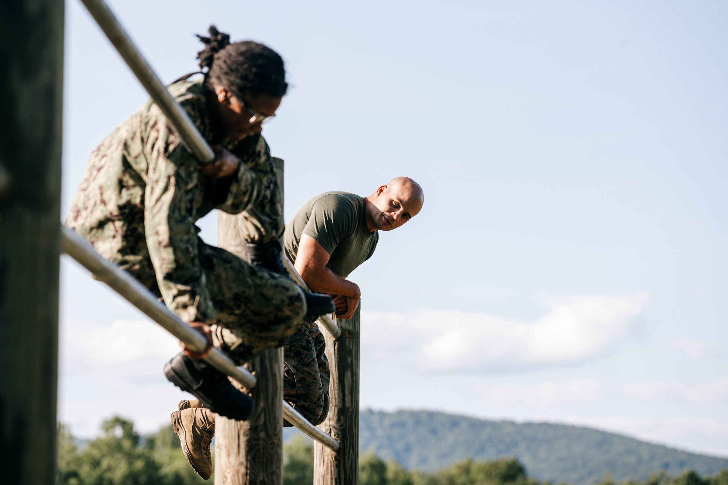 Candid photo of U.S. Marine Gunnery Sgt. Vernon Ditaranto, right, one of the career Marines overseeing the candidates’ training, observes as Candidate Briana Bozeman surmounts a barrier on the obstacle course.