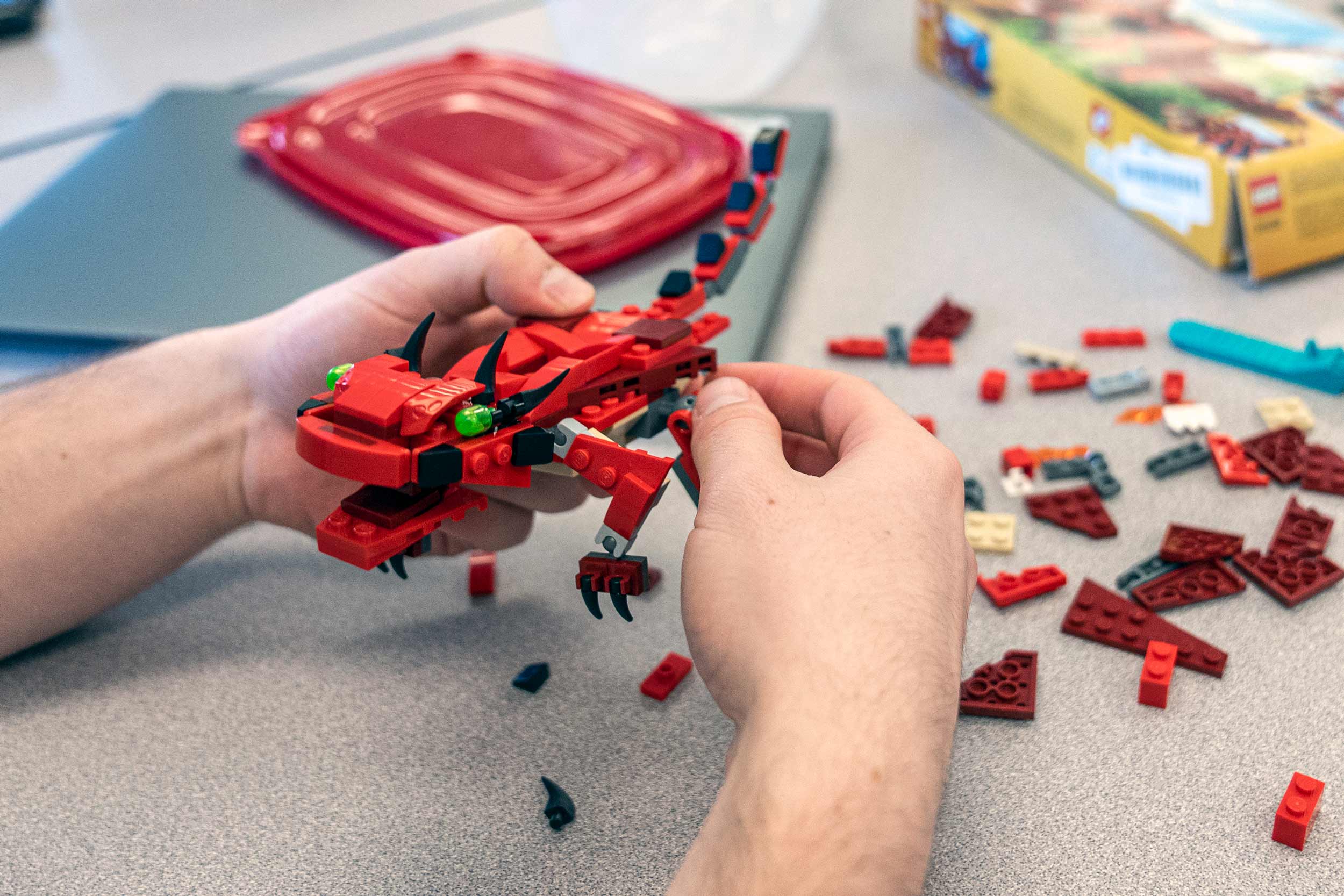 Close up of hands building a red dragon out of Legos