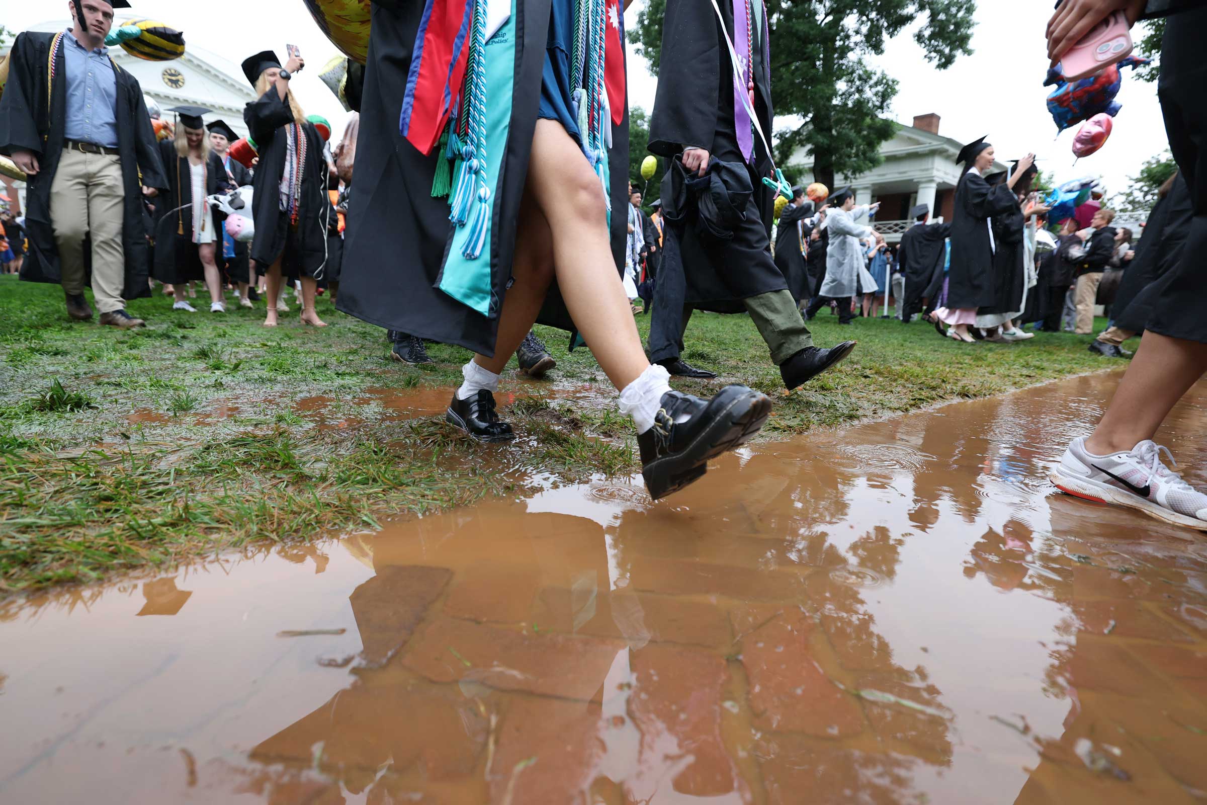 Close-up on the feet of graduating students walking down a muddy Lawn