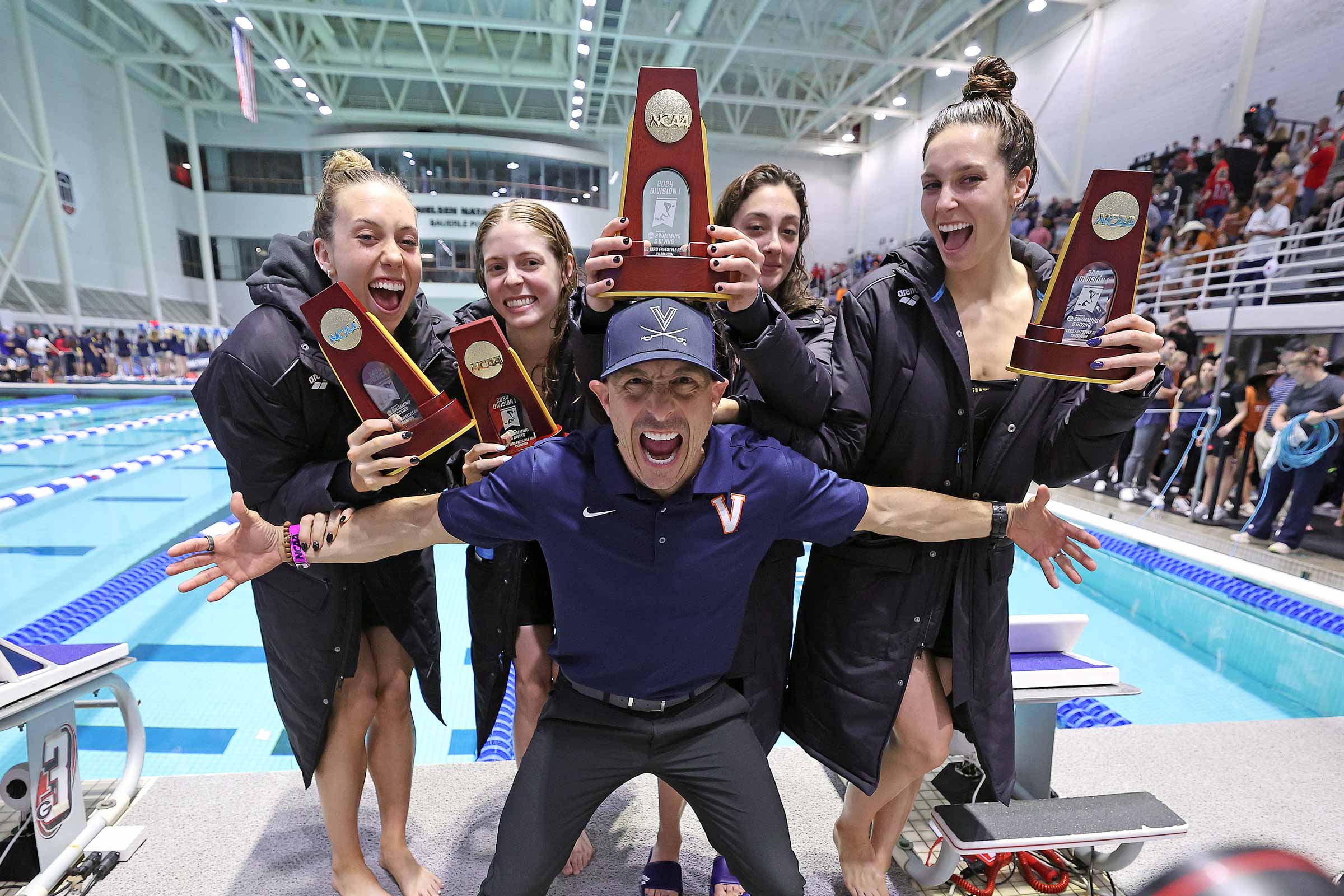 Coach poses in front of swimmers holding trophies