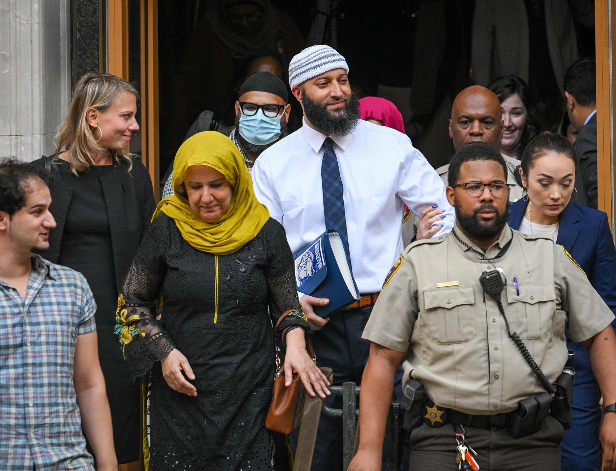 People walk out of a prison behind a prison guard.