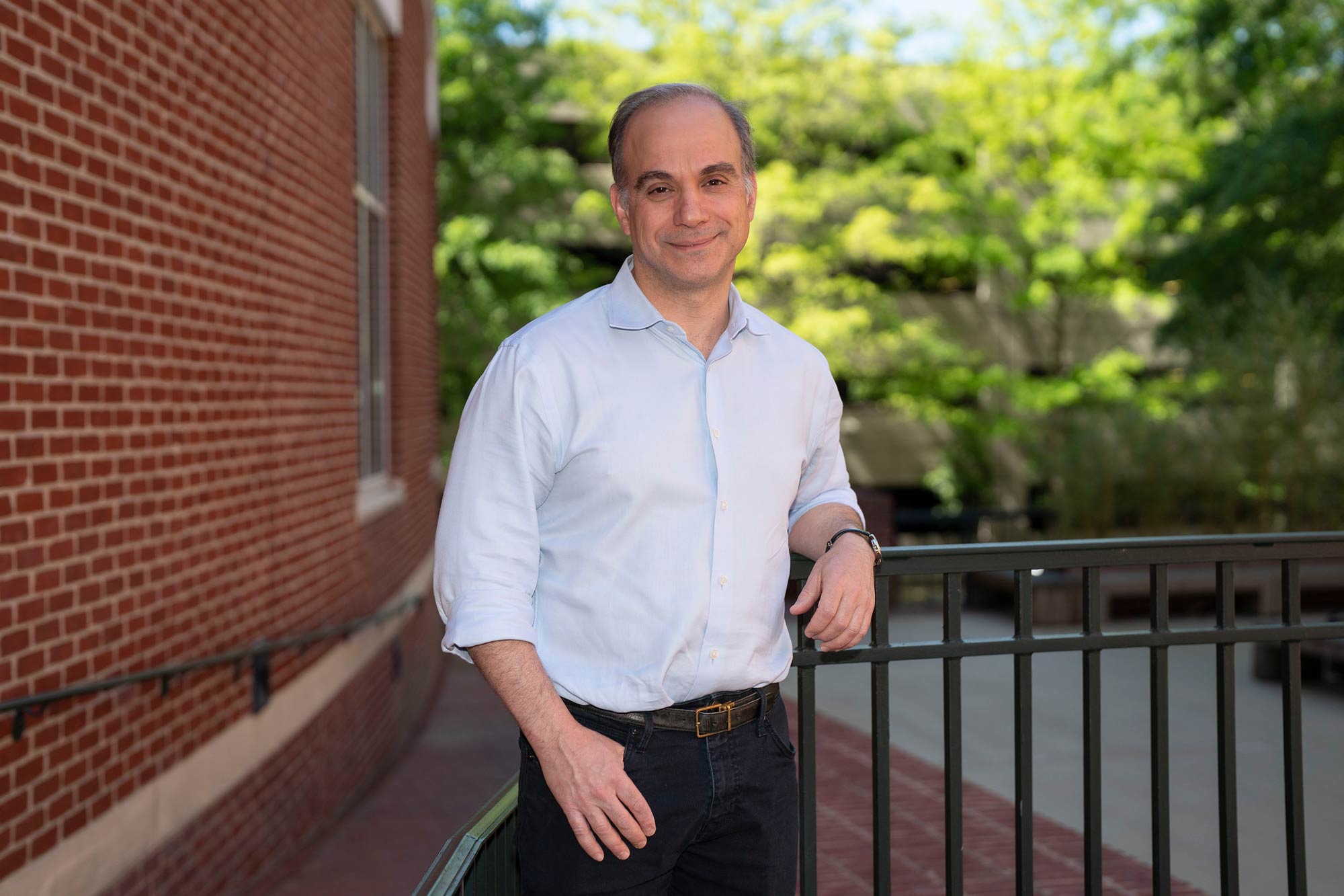 James Zimring leans on an iron railing beside a brick building and smiles at the camera