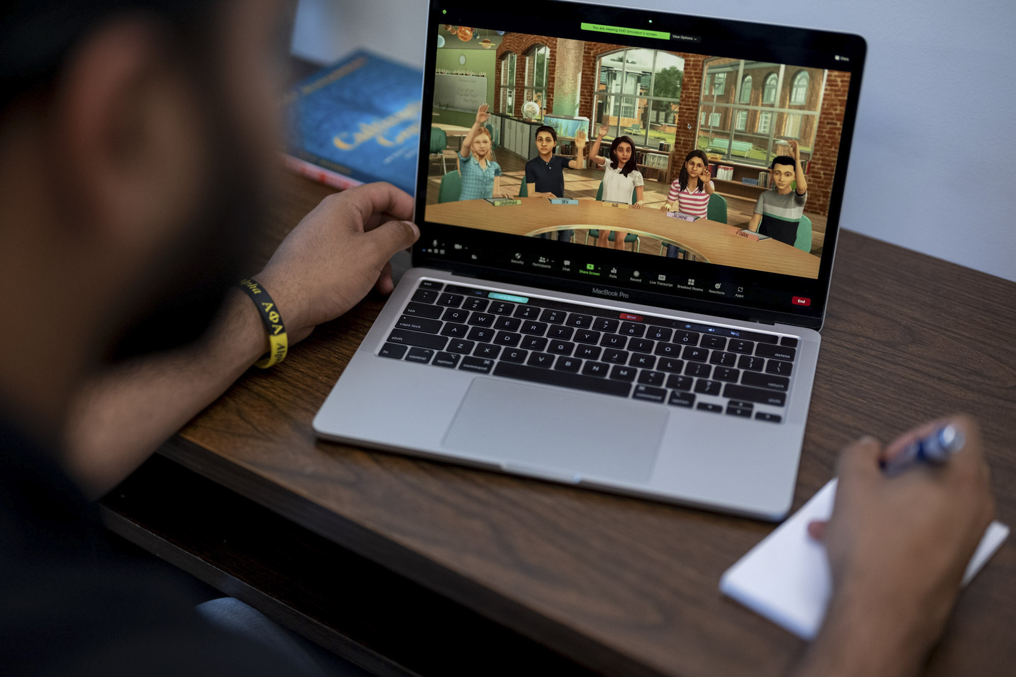 Over Jayden Bolden's shoulder, a laptop with virtual children in a zoom meeting