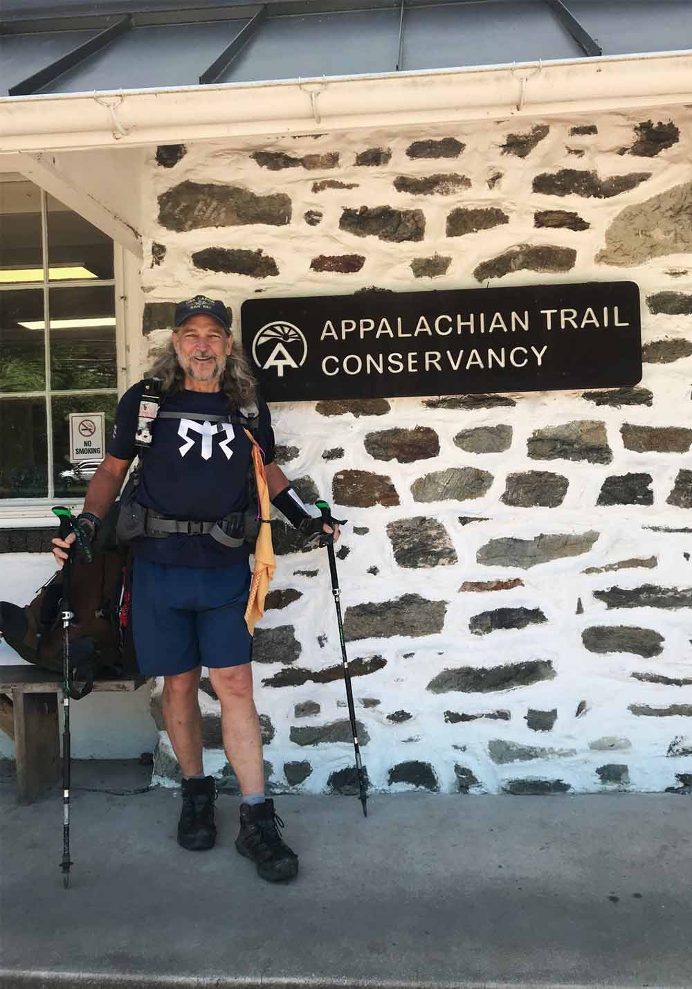 Tim Richard stands in front of a stone building, with a sign reading Appalachian Trail Conservancy