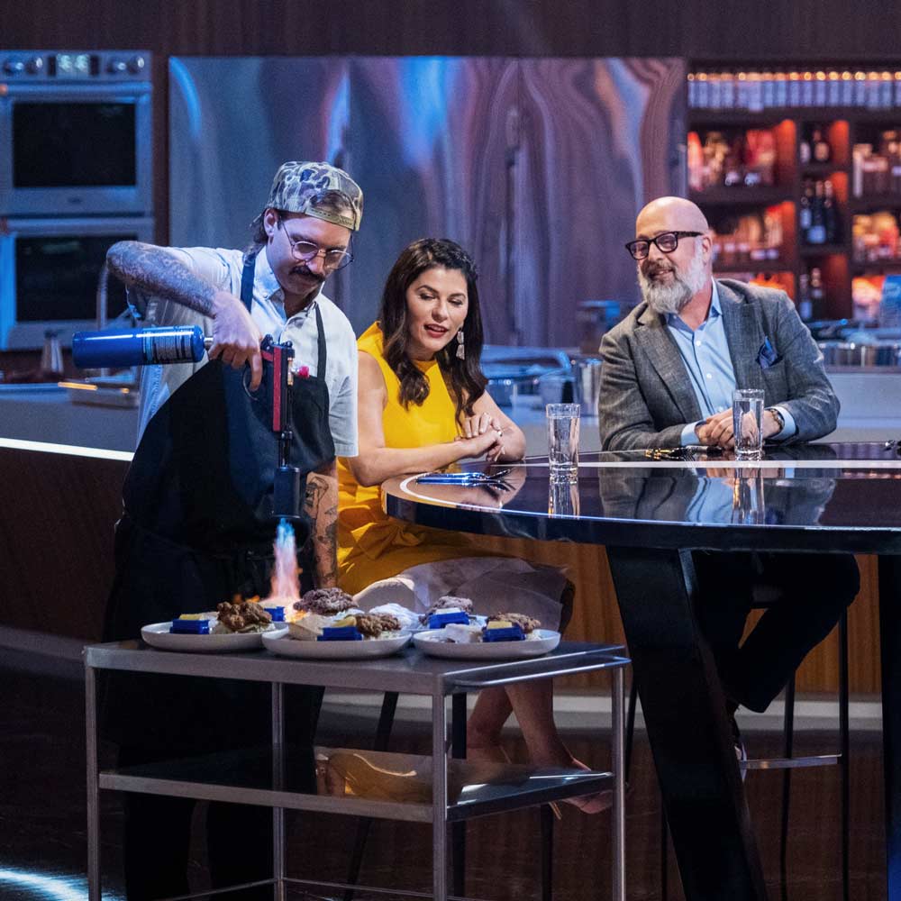 Hereford blowtorches three dishes in front of two judges on the set of Iron Chef