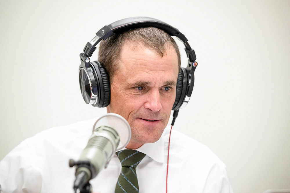 Jim Ryan wears headphones and talks into a microphone