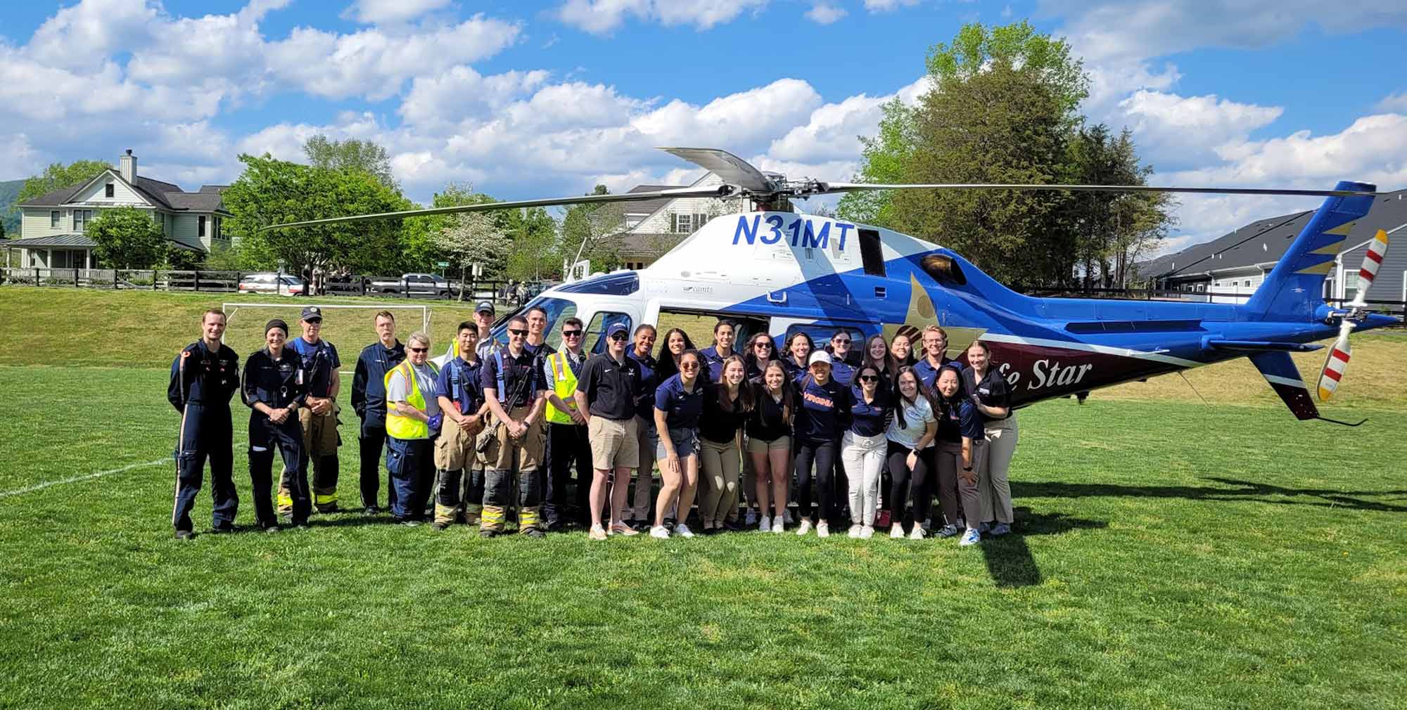 A group gathers in front of a helicopter for a photo