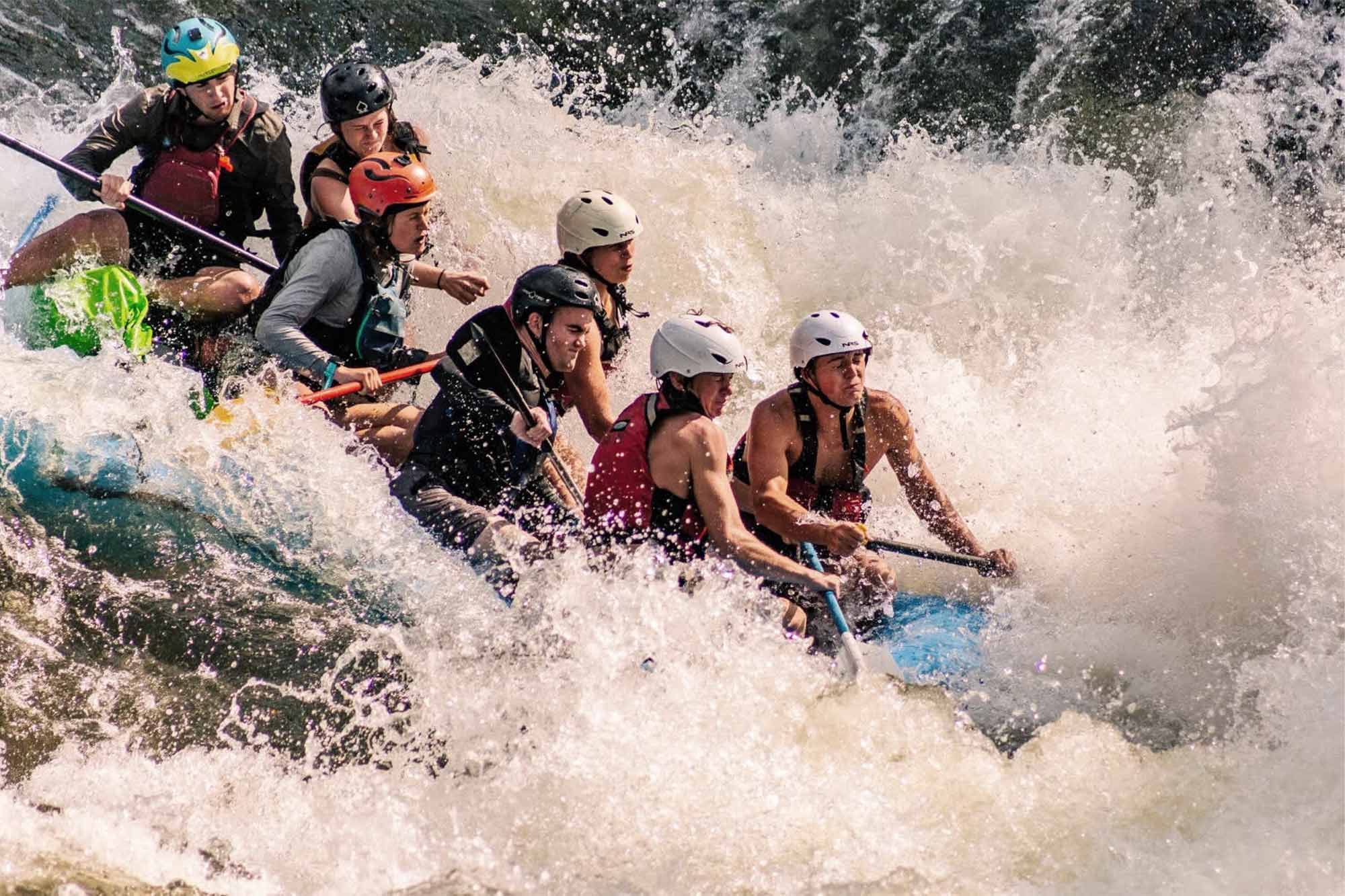 Seven students in helmets are whitewater rafting