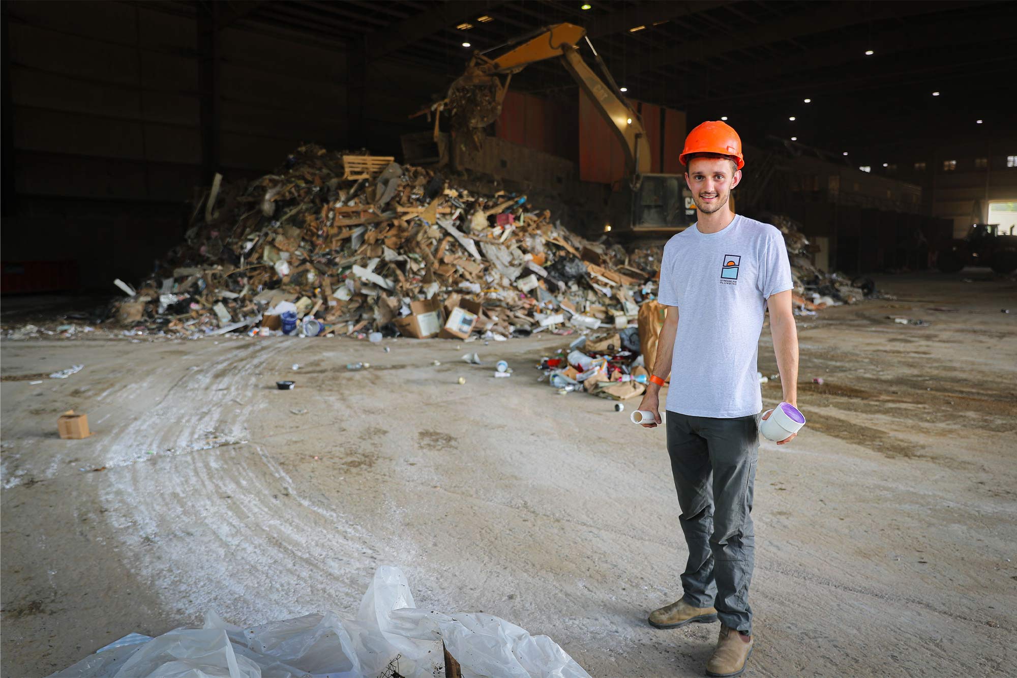 Levi Otis wears an orange hard hat and stands in front of a pile of refuse