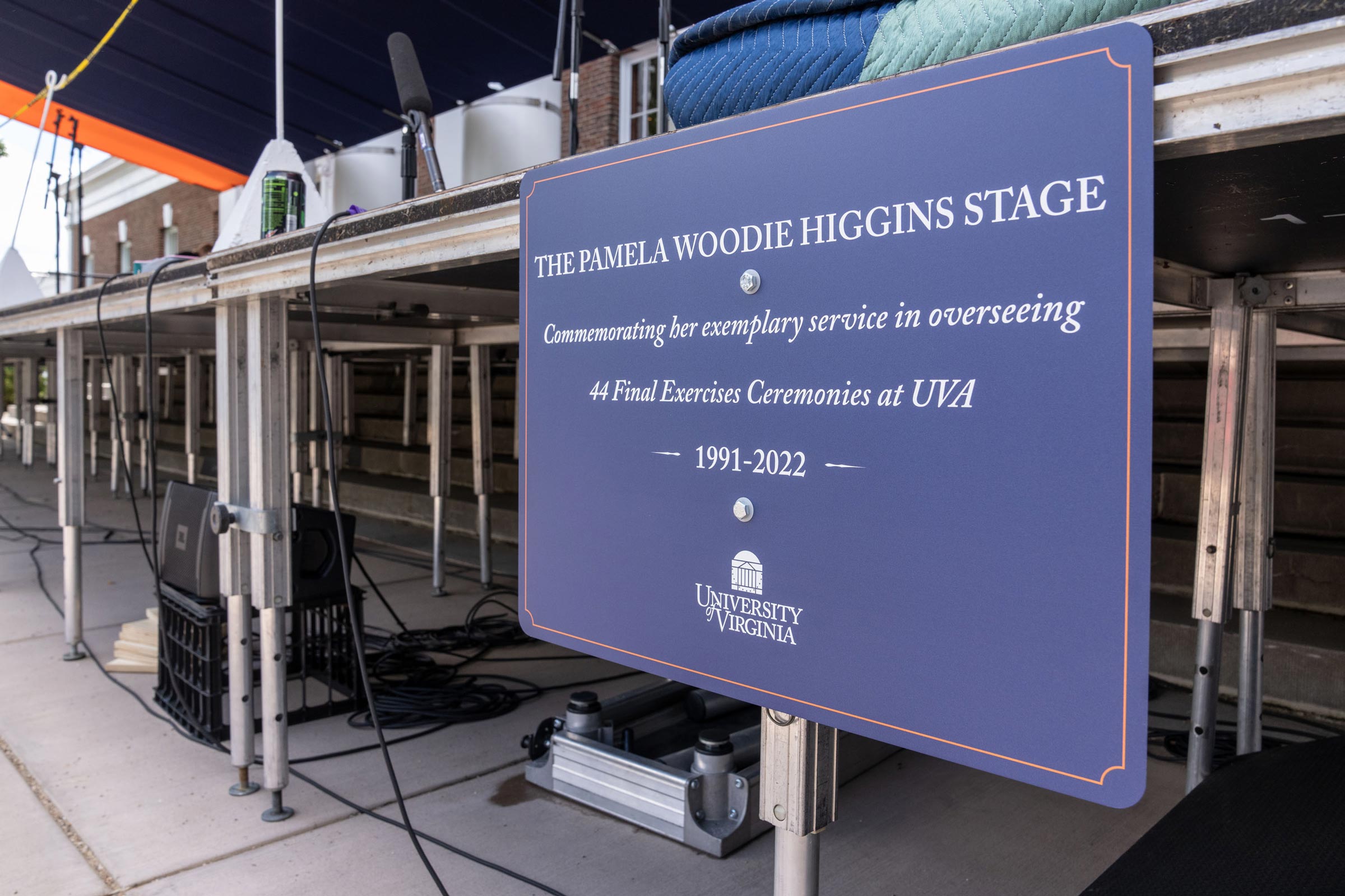 A sign on a stage reads 'The Pamela Woodie Higgins Stage. Commemorating her exemplary service in overseeing 44 Final Exercises Ceremonies at UVA 1991-2022.'