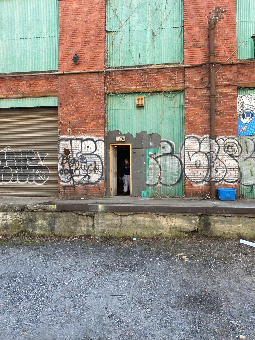 A man in a mask standing in an open doorway of a graffitied industrial building